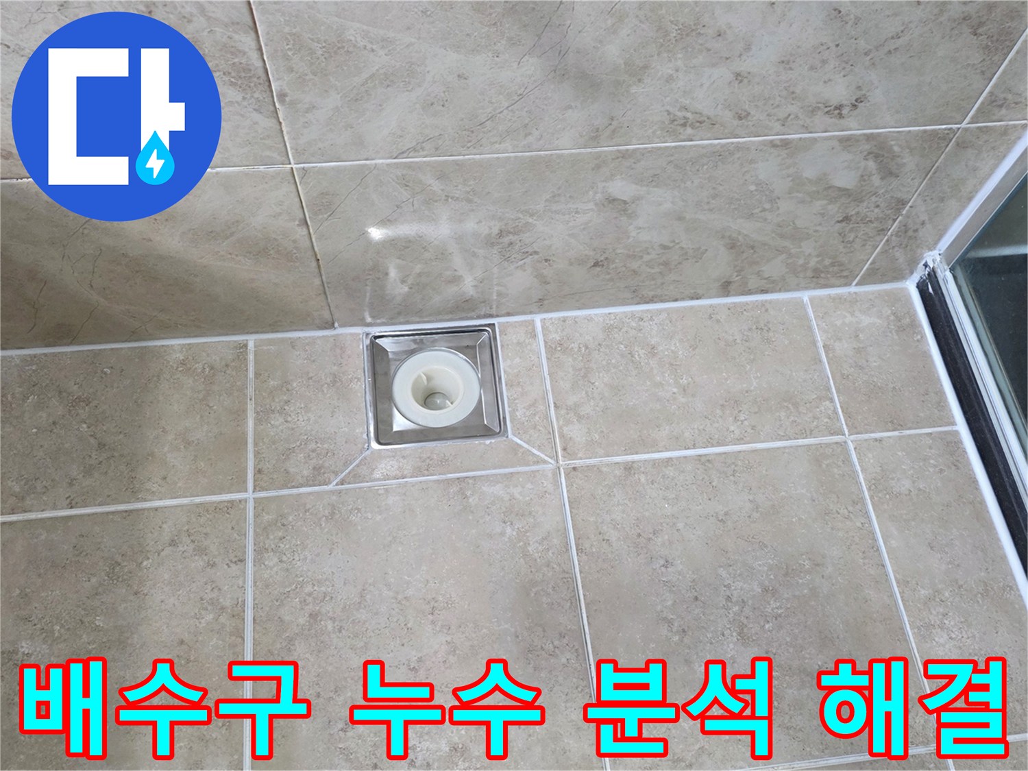 베이지색 타일 바닥에 설치된-사각형 금속 배수구의 모습으로-주변 타일과 줄눈의 상태를 면밀히 관찰하는 이미지입니다