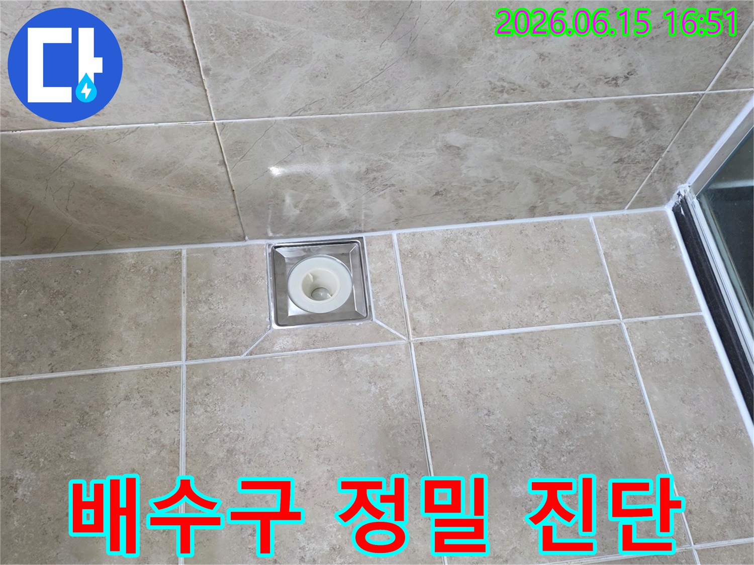욕실 바닥에 설치된-사각형 스테인리스 배수구-주변 타일과 백시멘트 마감 상태를 보여주는 이미지입니다