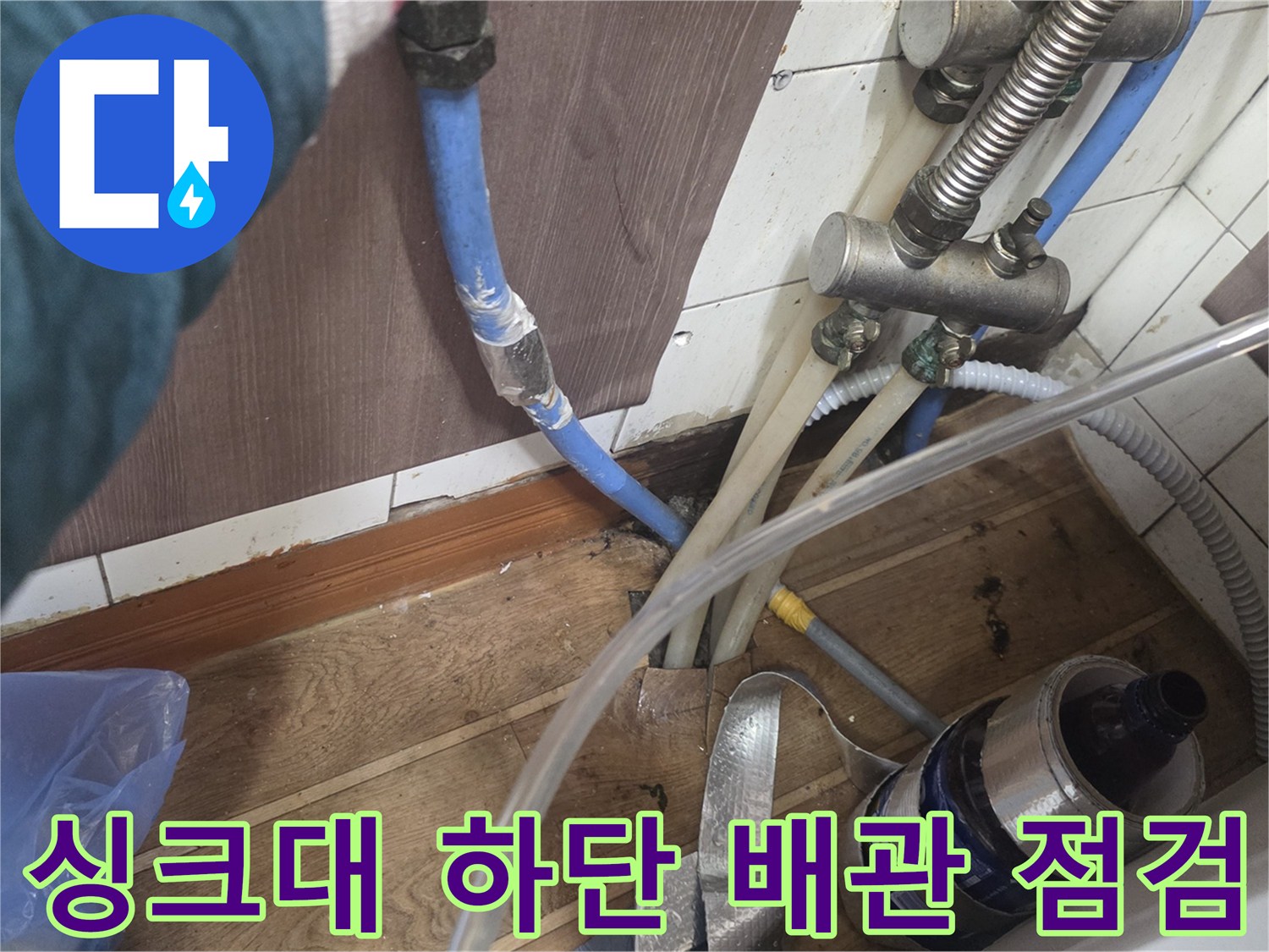 파란색 온수 배관과 금속 부속품이 보이는 싱크대 아래 공간