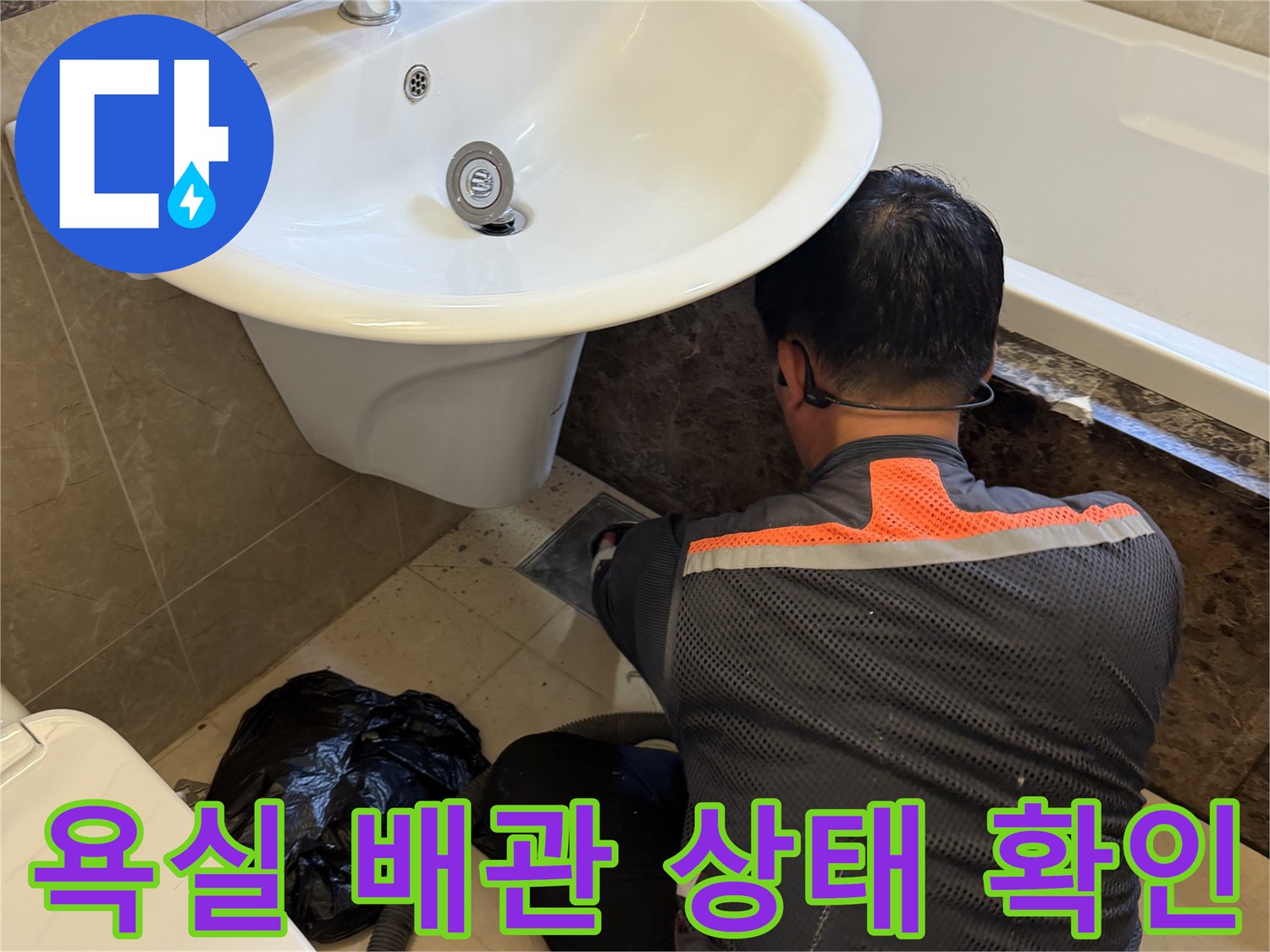 세면대 아래 공간에서 배수구 주변의 오염이나 틈새를 점검하는 작업자입니다.