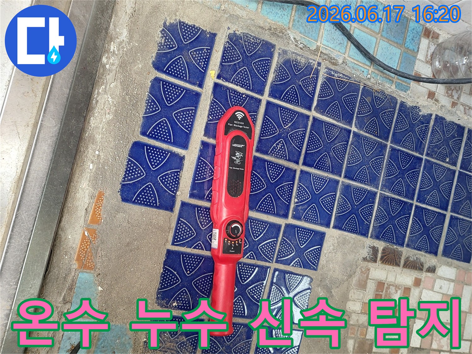 파란색 타일이 뜯겨나간 욕실 바닥에 놓인-붉은색 누수탐지 장비가-온수 배관 누수 지점을 신속히 찾는 중인 모습