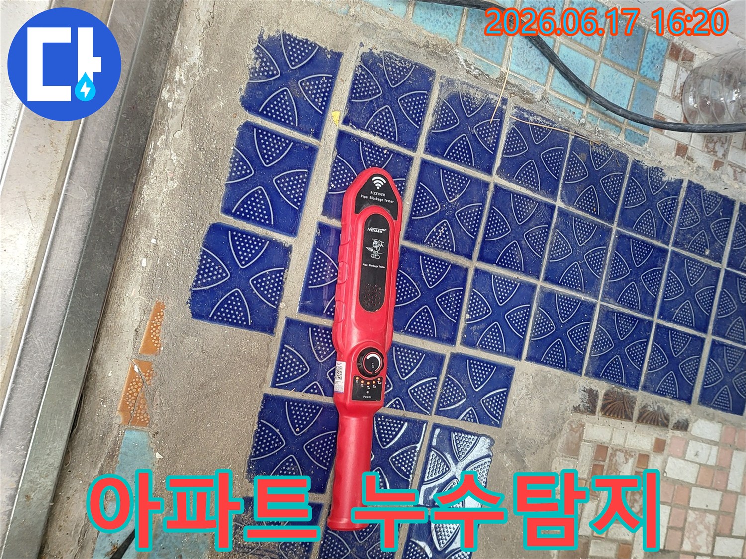 파란색 타일이 부분적으로 제거된 아파트 욕실 바닥에-붉은색 누수탐지 장비가 놓여-누수 지점을 찾는 중인 모습