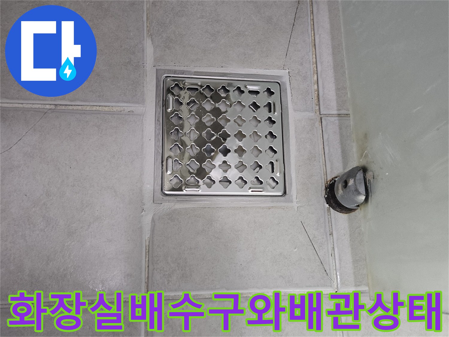 욕실 배수구 주변의 타일 균열과 노출된 배관 상태를 보여주는 사진입니다.