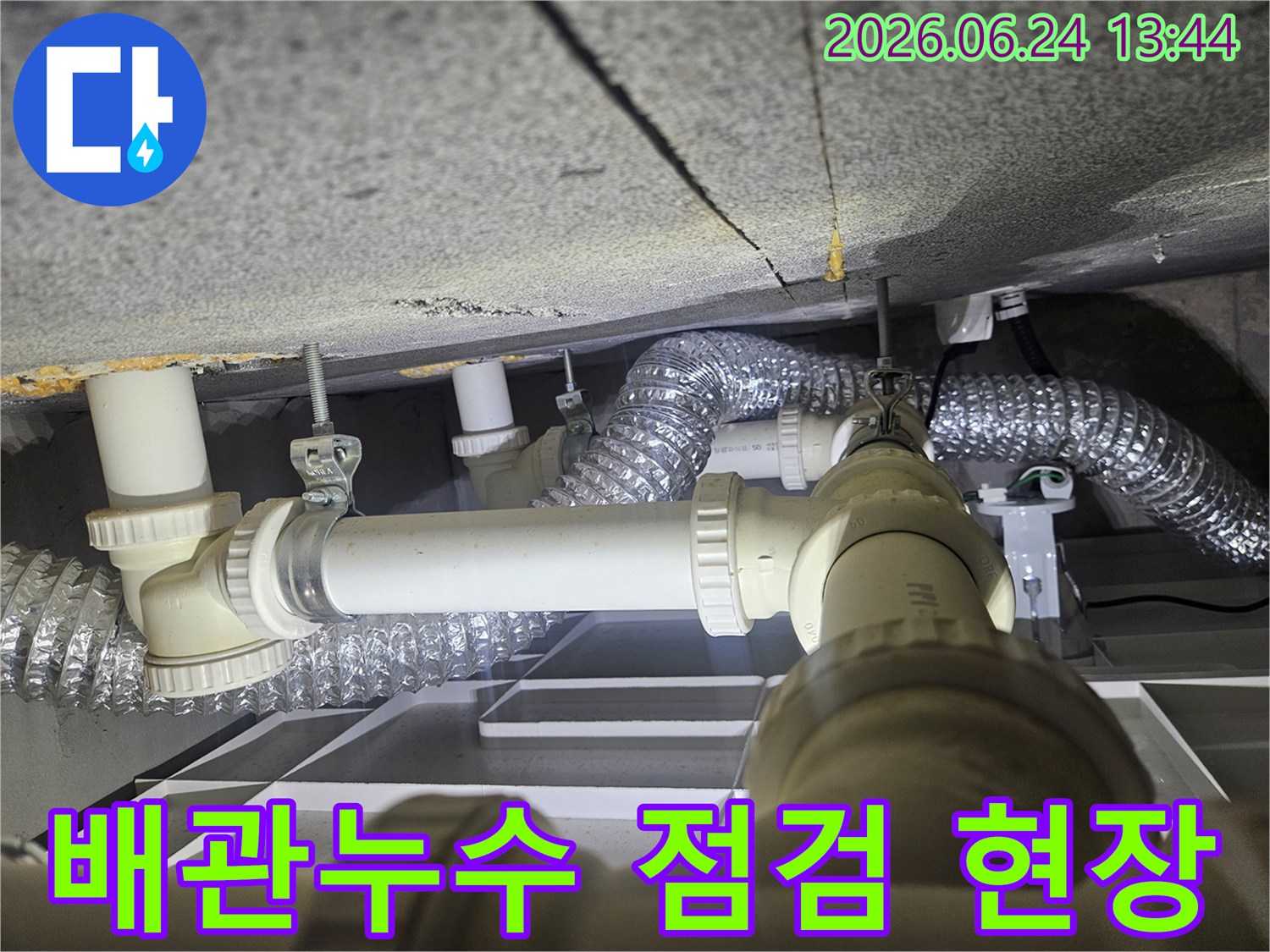 천장 아래 복잡하게 얽힌 배관과-환기 덕트를-누수 전문가가-꼼꼼히 점검하는 모습입니다