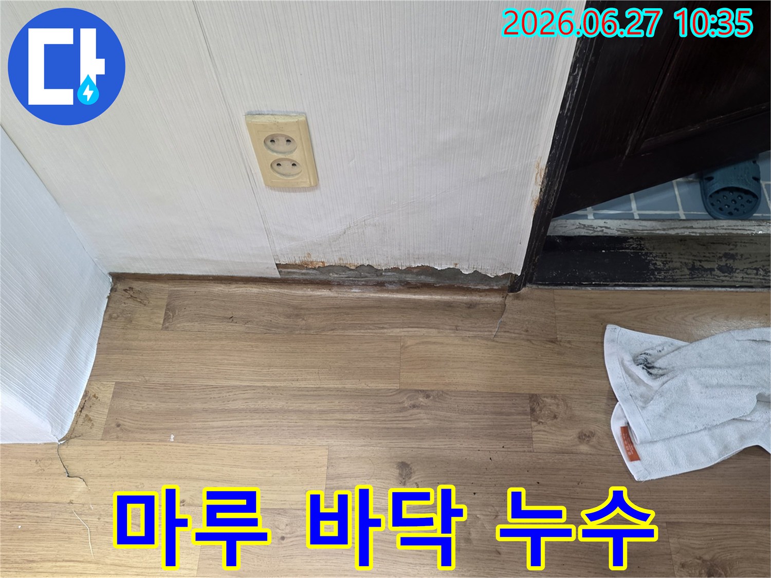벽면 하단과 마루 경계 부분에 물기가 스며들어-변색되고 손상된 누수 현장의 모습입니다.