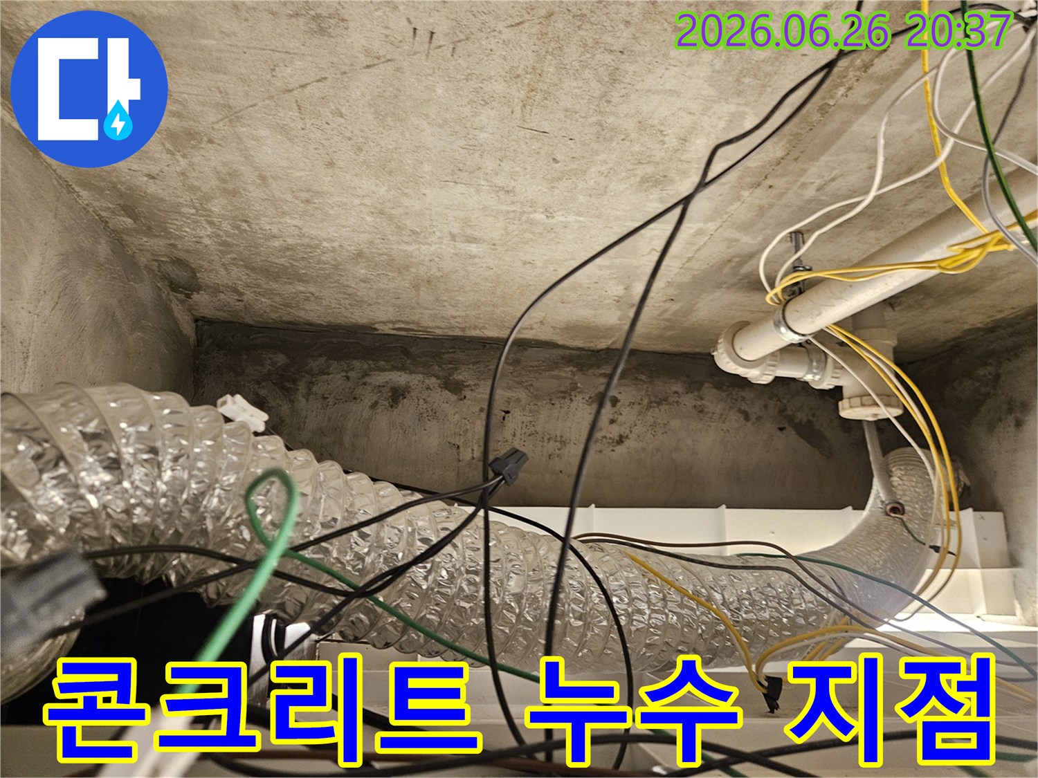 이 이미지는 천장 콘크리트 벽면의-어두운 변색과 습기 흔적-그리고 주변의 배선 및 덕트를 통해-누수 지점을 보여줍니다.