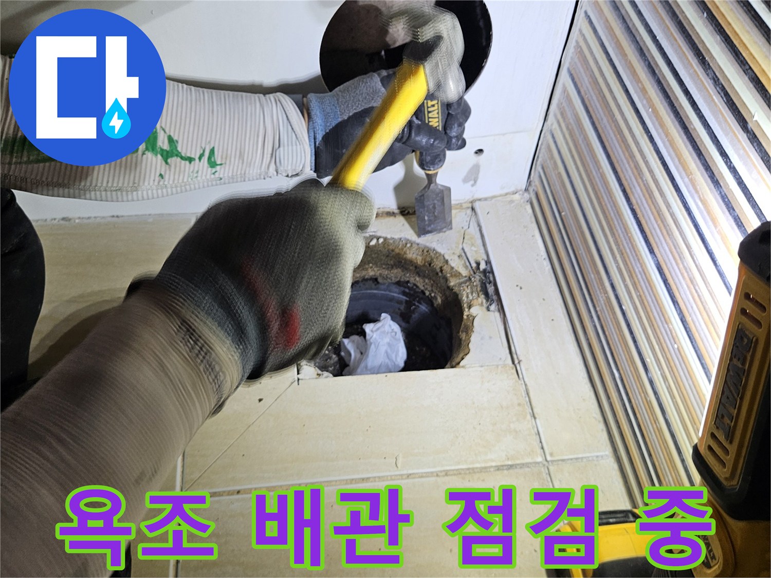 장비를 사용하여 욕조 옆면 타일을 제거하고 내부를 들여나다보는 장면입니다.