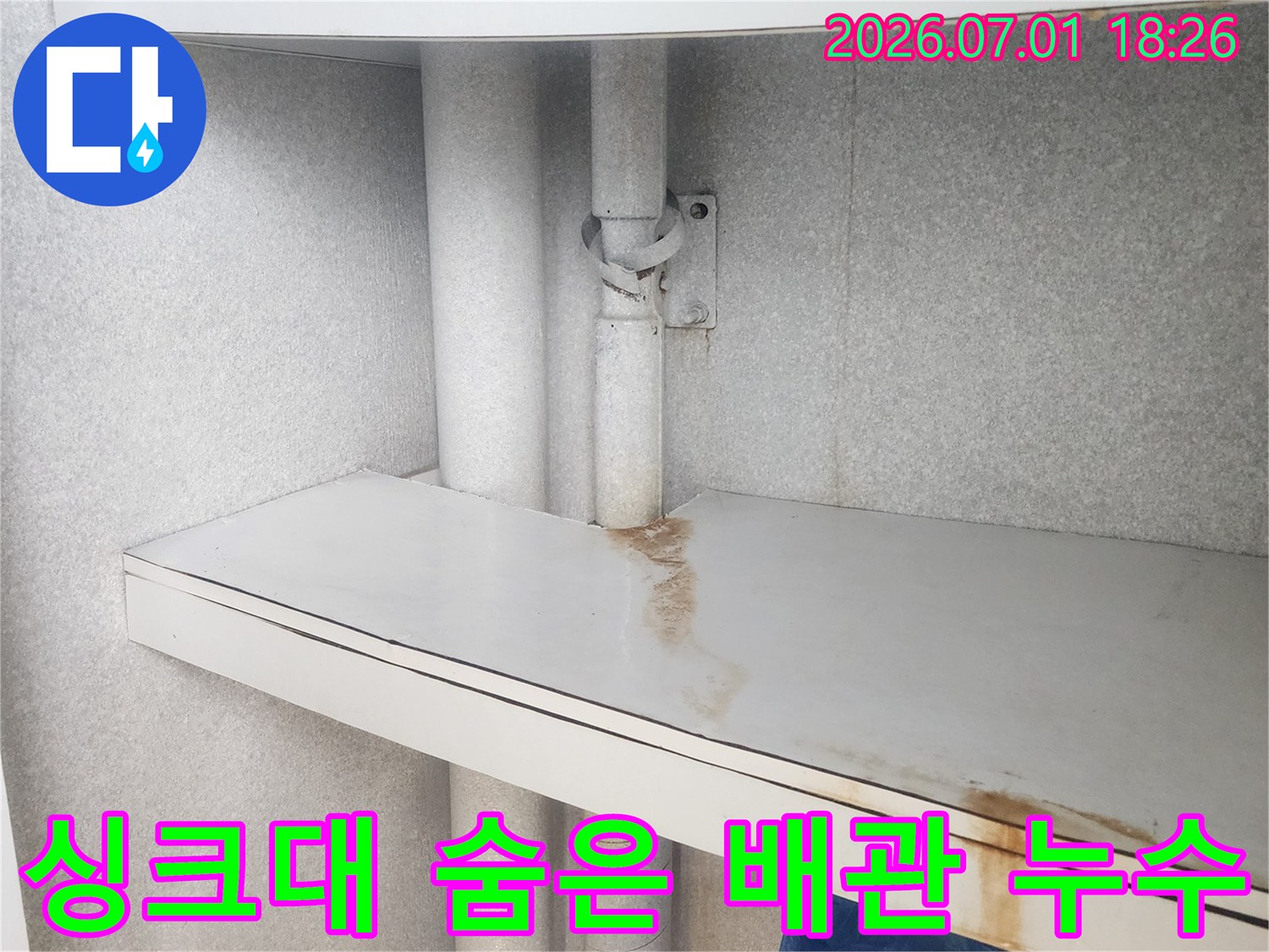 이 이미지는-싱크대 하부-가구 패널에-나타난-오래된 누수로 인한-물 자국과-배관의 모습을-상세히 보여줍니다