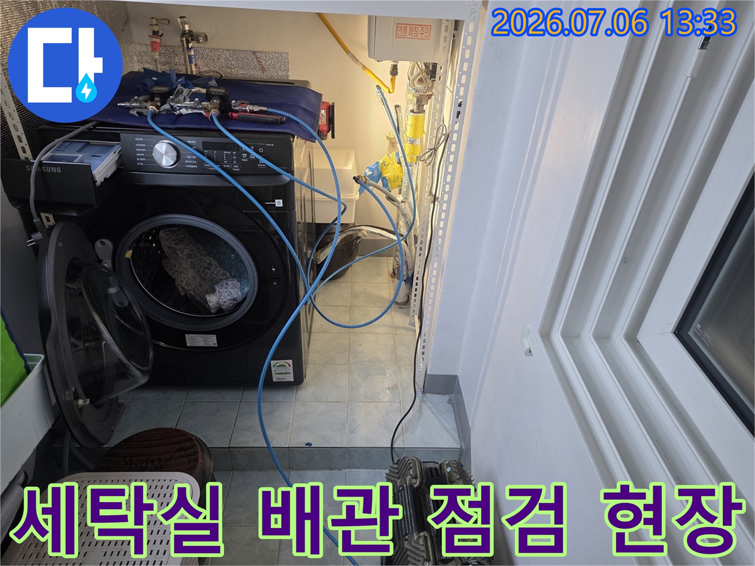 세탁기 옆에 위치한 복잡한 배관과 계량기가 설치된 세탁실 내부 모습