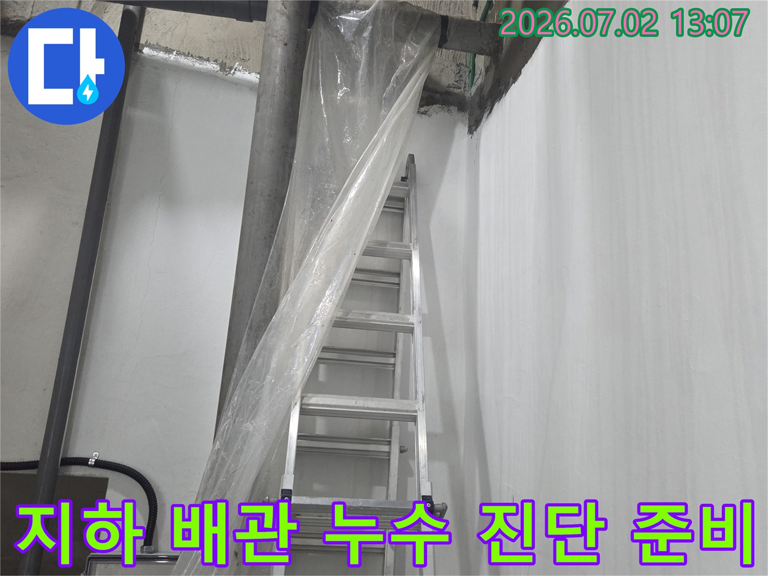 천장에 설치된 여러 가닥의 회색 하수 배관과 그 아래 배치된 작업용 사다리