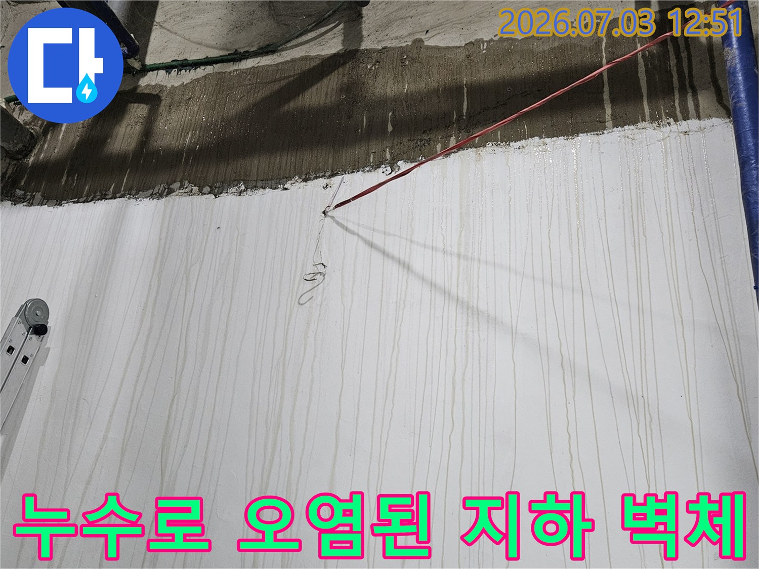 흰색 벽면에 수직으로 형성된 누수 얼룩과 상단 배관 및 콘크리트 구조물