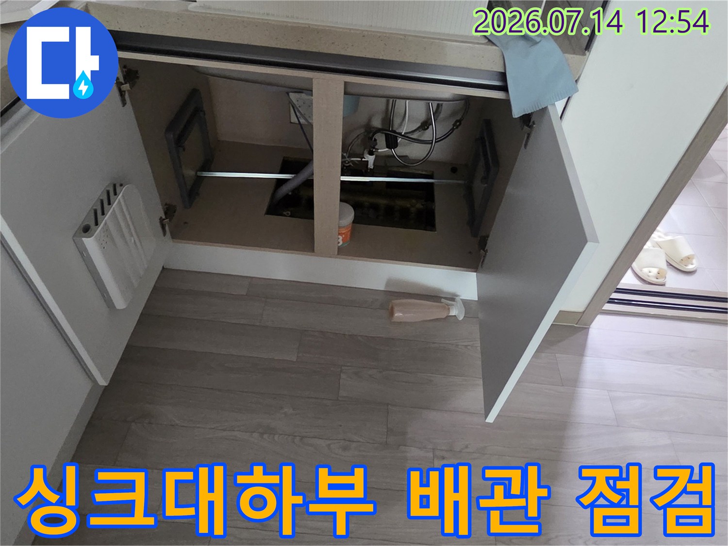 싱크대 하부장을 열고 노출된 수도 배관과 연결 부위를 정밀하게 점검하는 모습