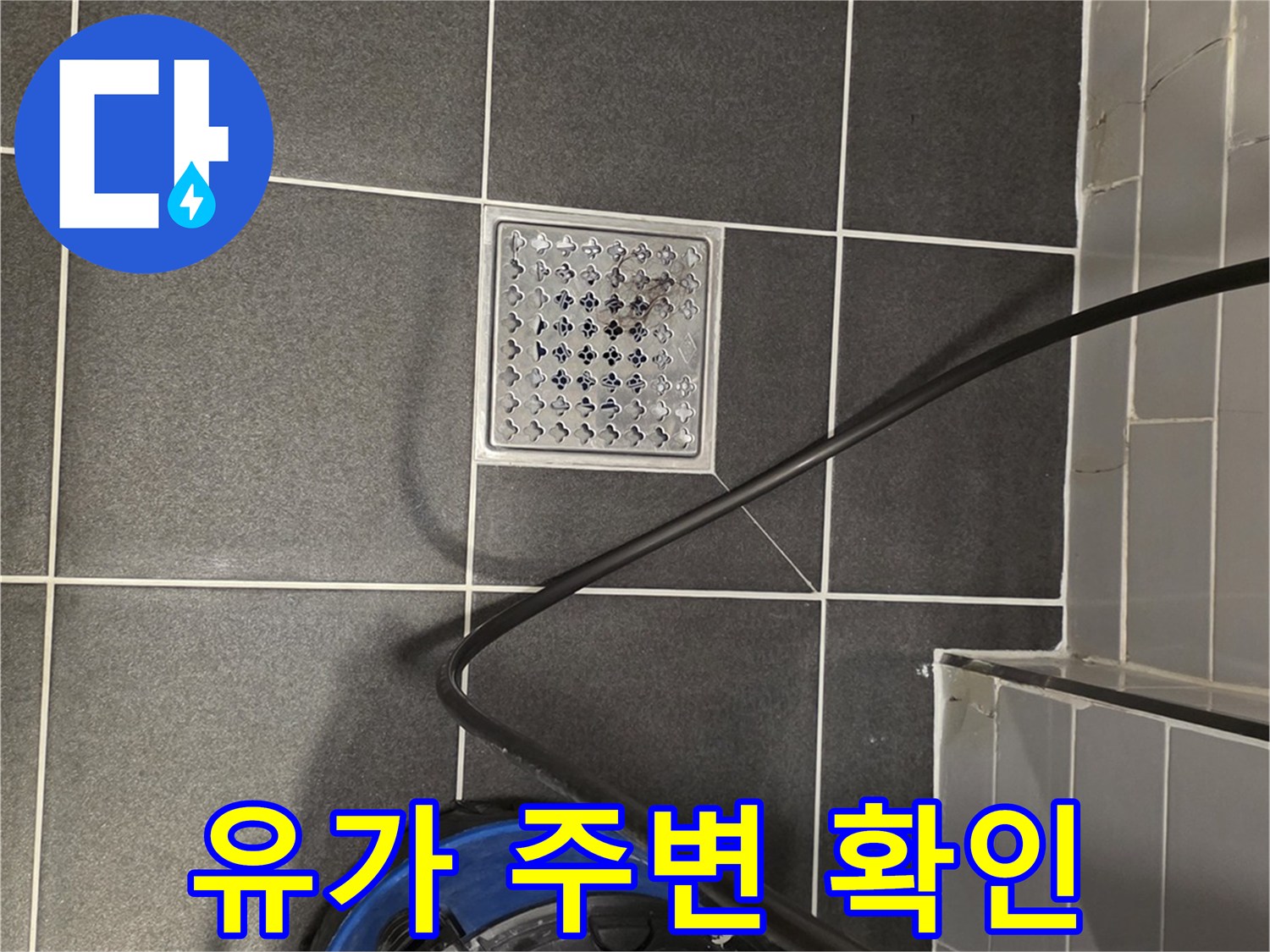 화장실 바닥의 금속 배수구와 청소용 진공청소기 모습