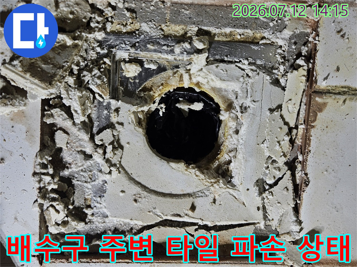 배수구 주변의 깨진 타일과 노출된 배관 부위