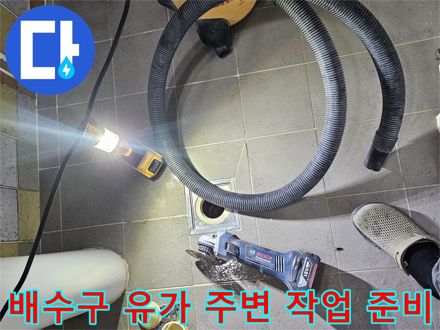 화장실 바닥의 배수구와 공구를 배치한 작업 현장 사진입니다.