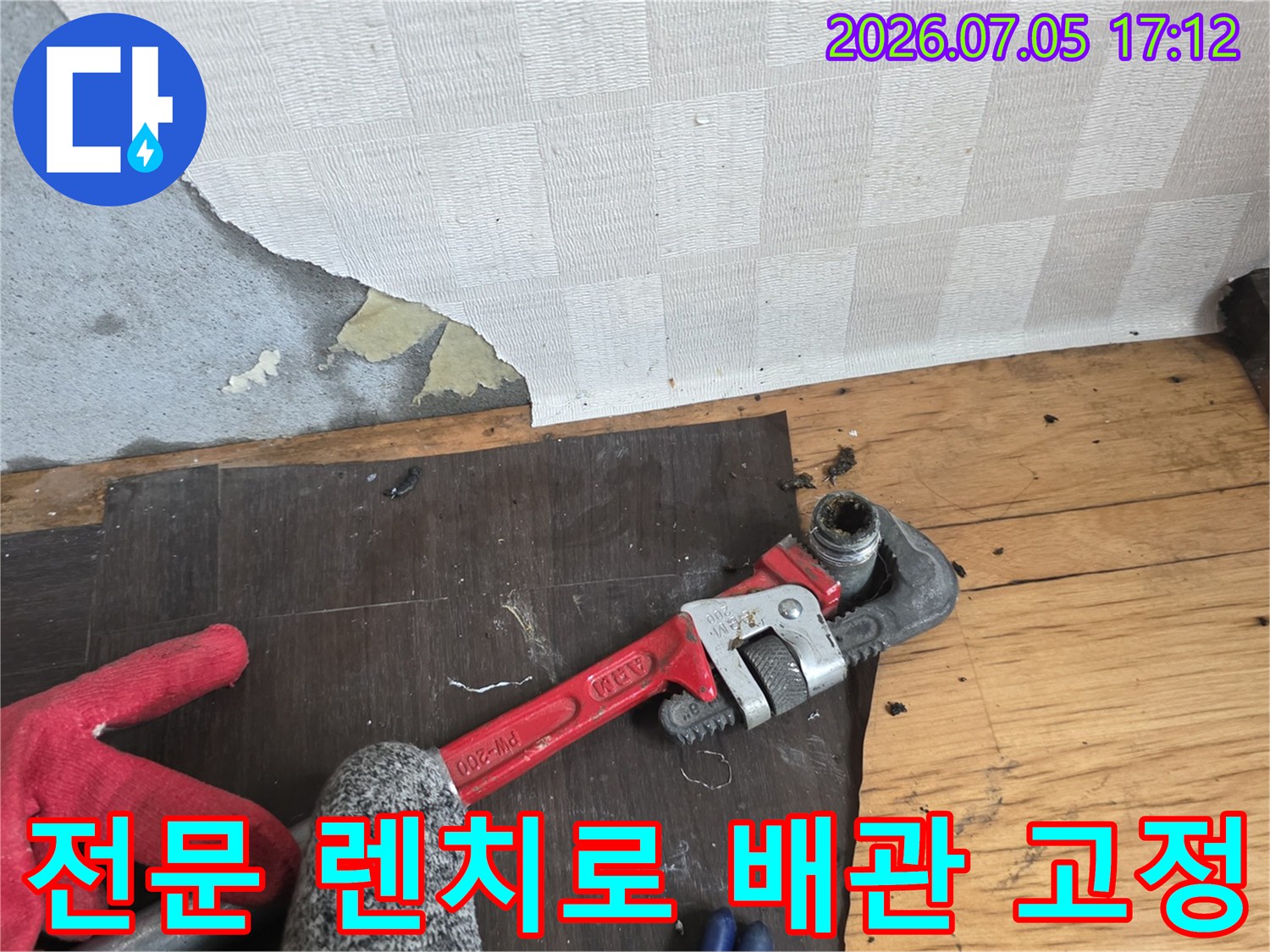 붉은색 렌치를 사용하여 수도 배관 연결부를 견고하게 조이는 작업 장면