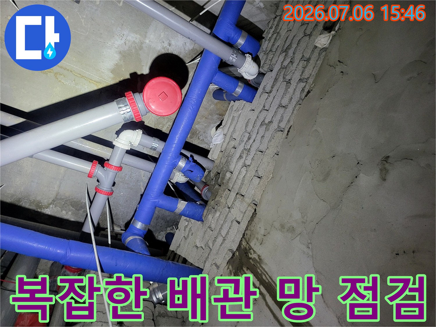 천장 내부 노출된 파란색 및 회색 배관들의 연결 상태를 정밀하게 진찰하는 장면