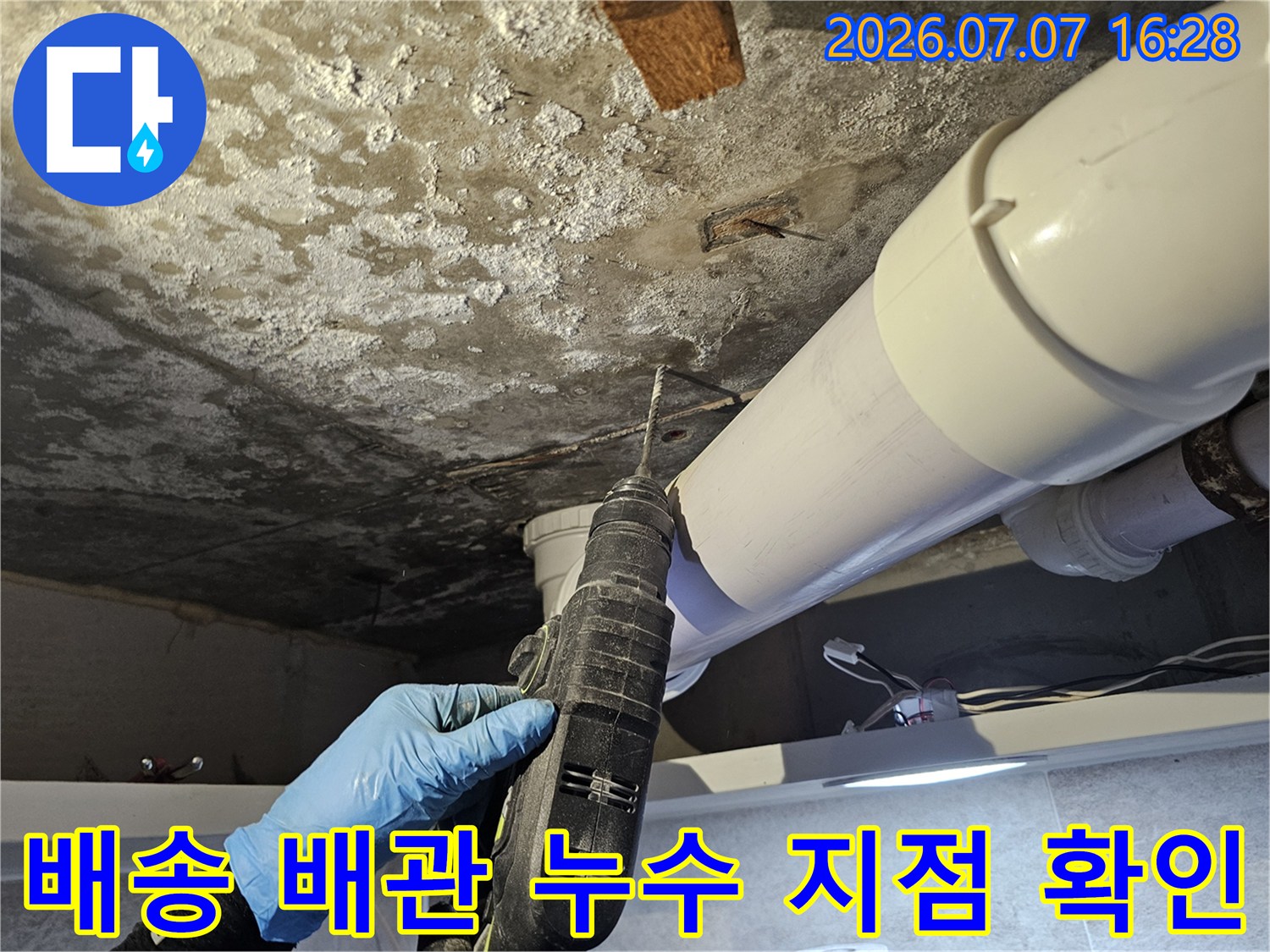 특수한 장갑을 끼고 천장 안쪽의 파손된 배출 배관을 조사하는 장면