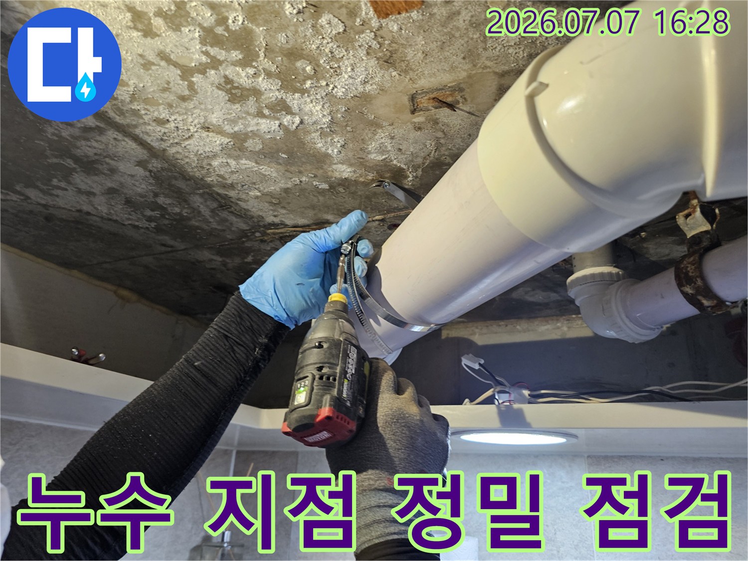 파란 장갑을 낀 작업자가 화장실 천장 배관의 연결 상태를 점검하는 모습입니다.