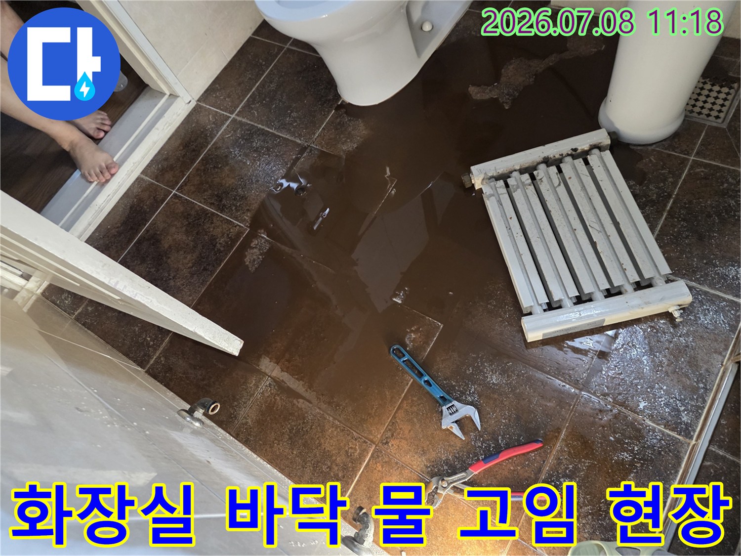 화장실 바닥에 물이 고여 있고 렌치와 라지에터가 놓여 있는 누수 점검 현장