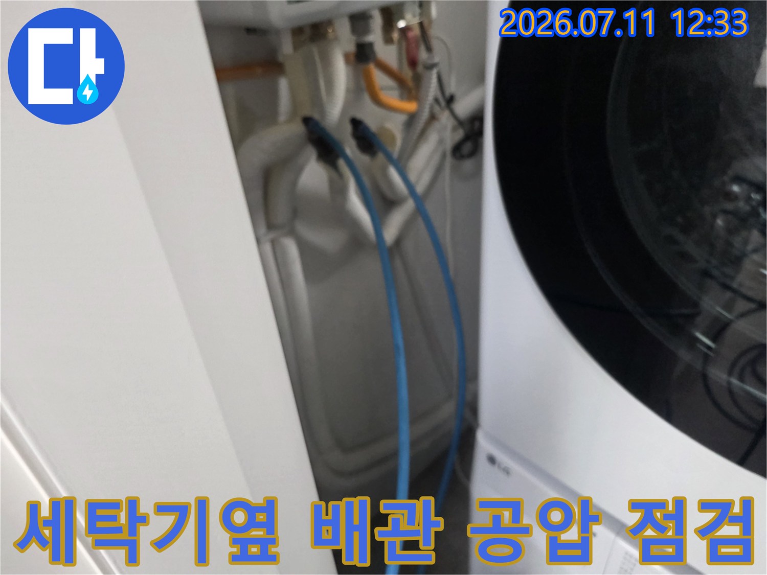 세탁기 옆에 위치한 배관에 공압 테스트 장비를 연결하여 기밀 상태를 확인하는 모습