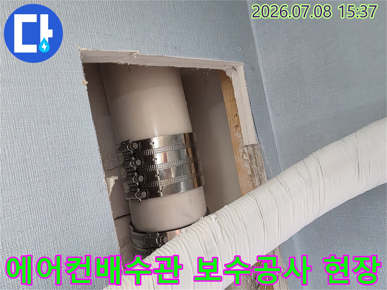 금속 밴드로 고정된 에어컨 배수관의 벽면 절개 점검 모습