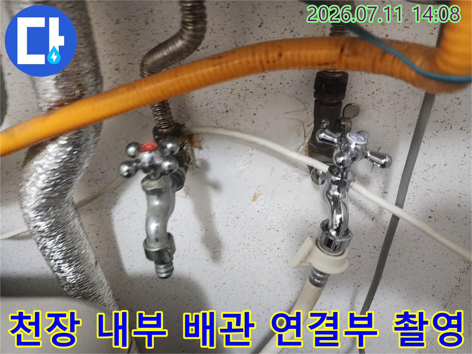 금속 밸브와 주황색 단열재가 노출된 천장 내 배관 시스템의 모습