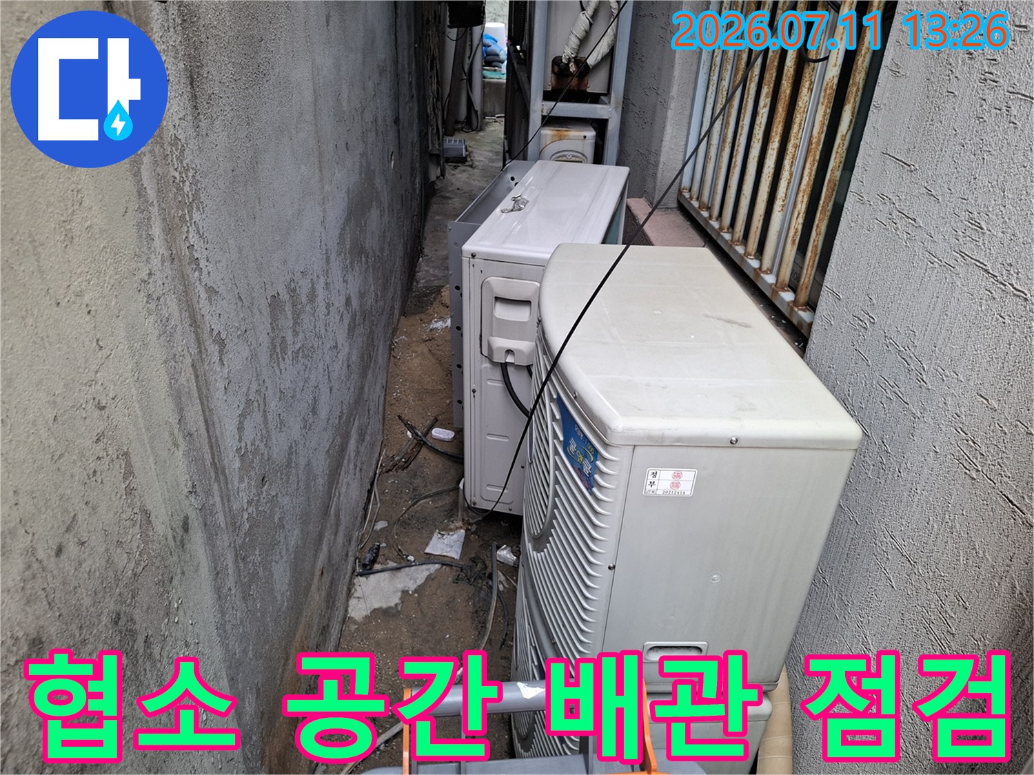 좁은 틈새에 위치한 에어컨 실외기 배수 시스템을 세심하게 확인하는 모습