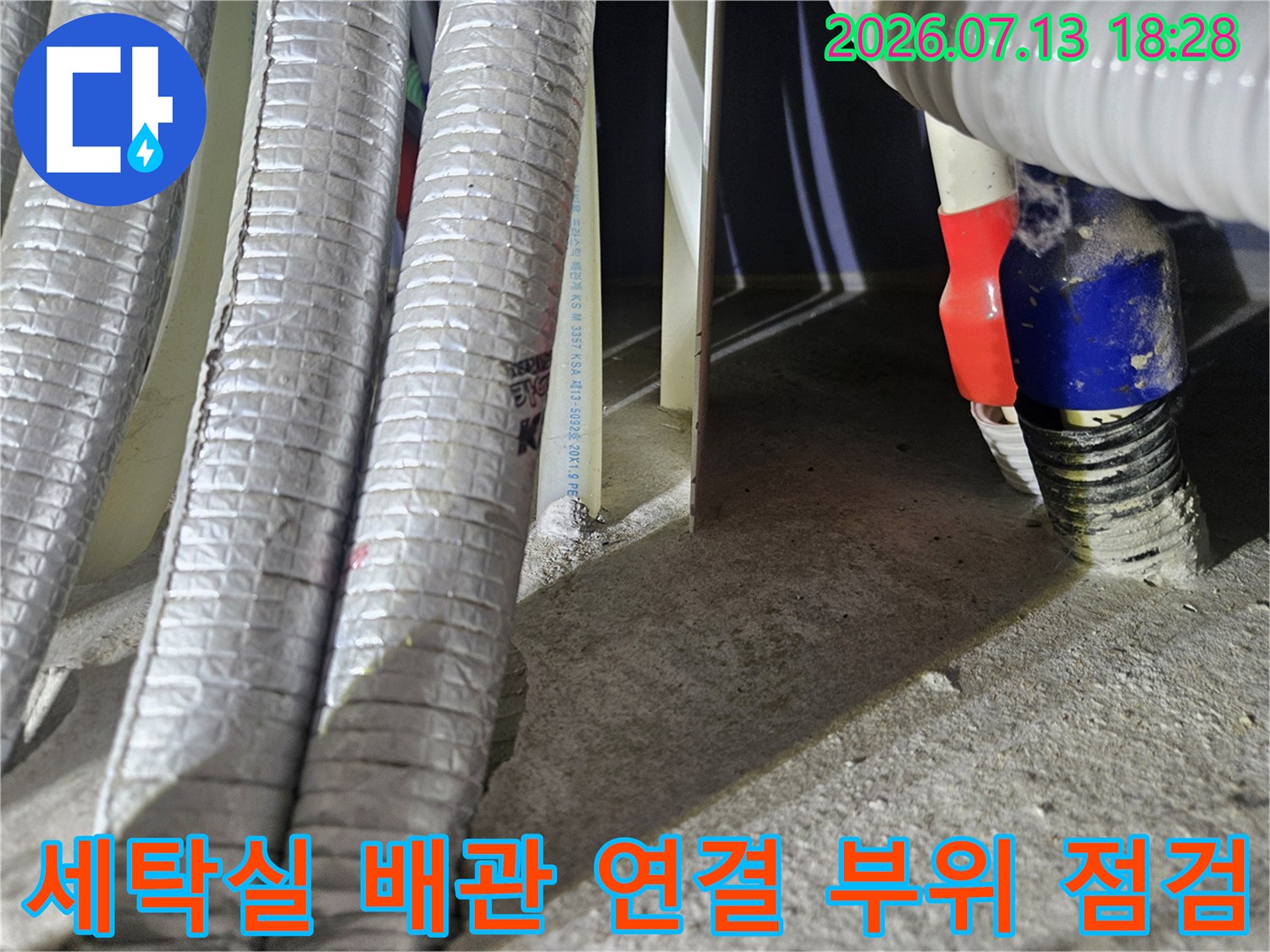 세탁실 바닥 하부의 은색 보온재로 감싸인 배관들과 파란색 밴드로 고정된 연결 부위