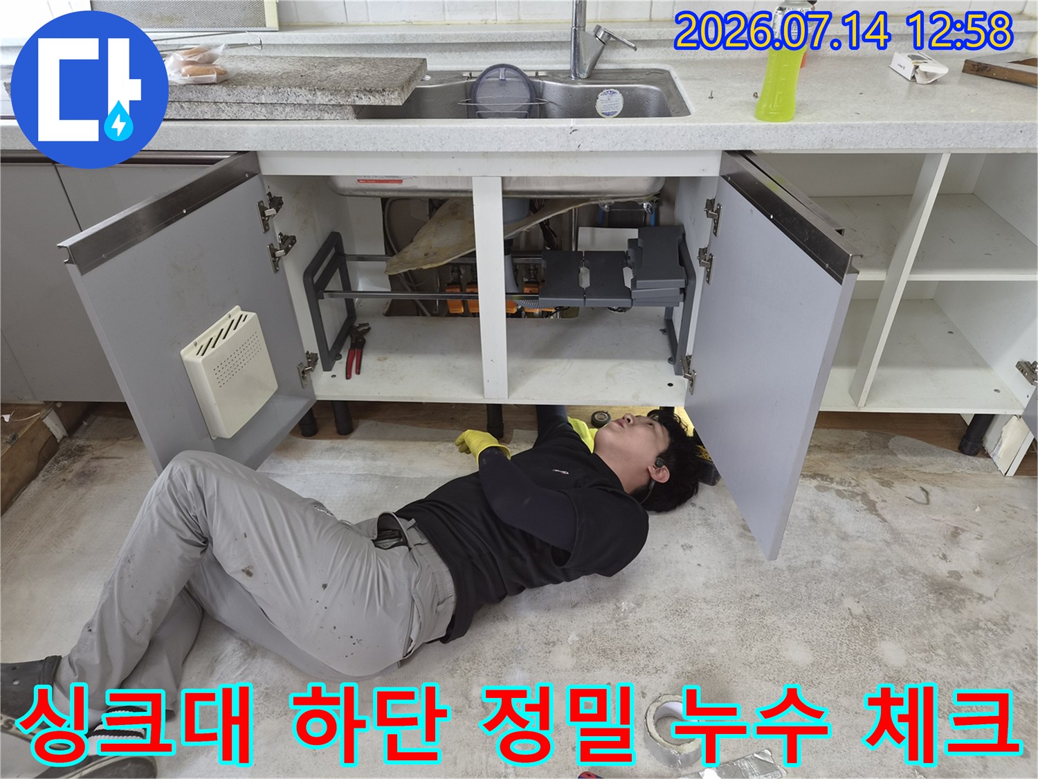 작업자가 싱크대 내부 배관-연결 부위를 면밀히 조사하는 모습