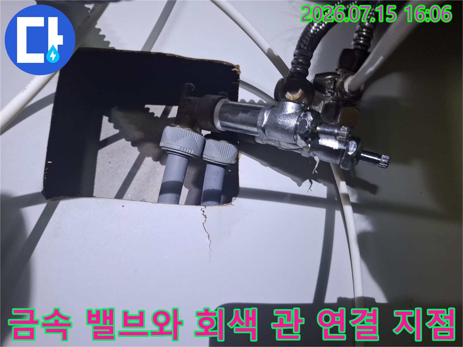 두 개의 회색 배관이 은색 금속제 밸브뭉치에 나사식으로 체결되어 있는 모습
