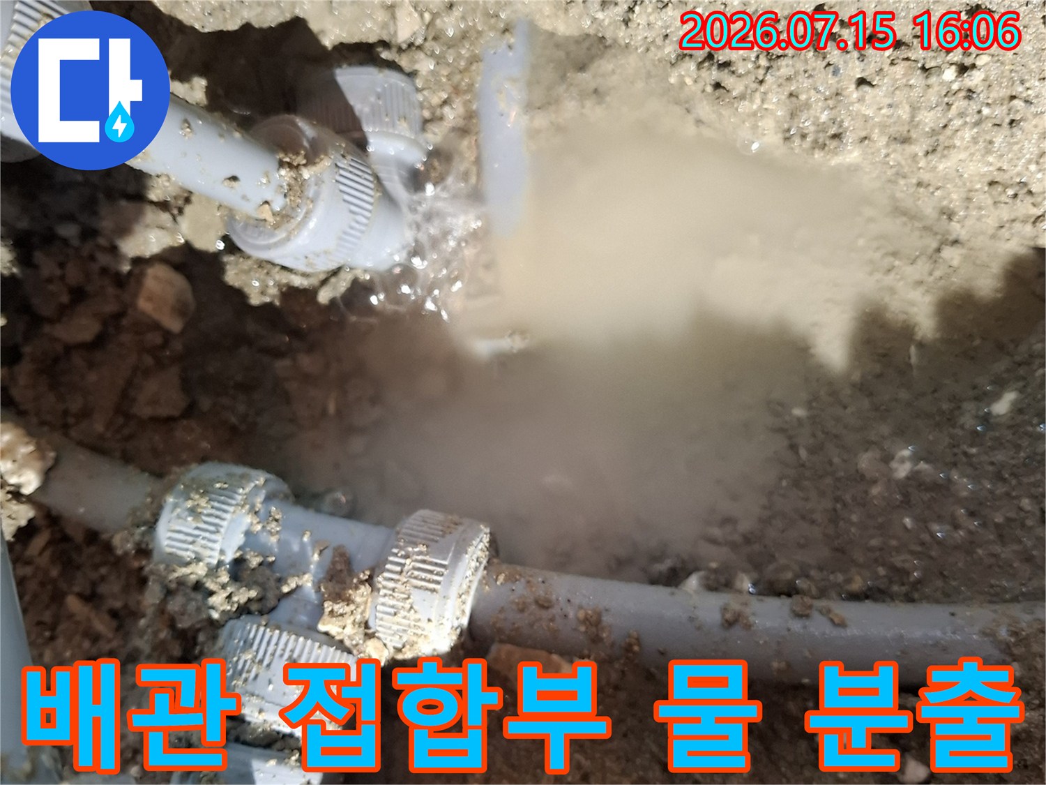 흙 속의 회색 플라스틱 배관 연결 부위에서 물이 세차게 뿜어져 나오는 현장 모습