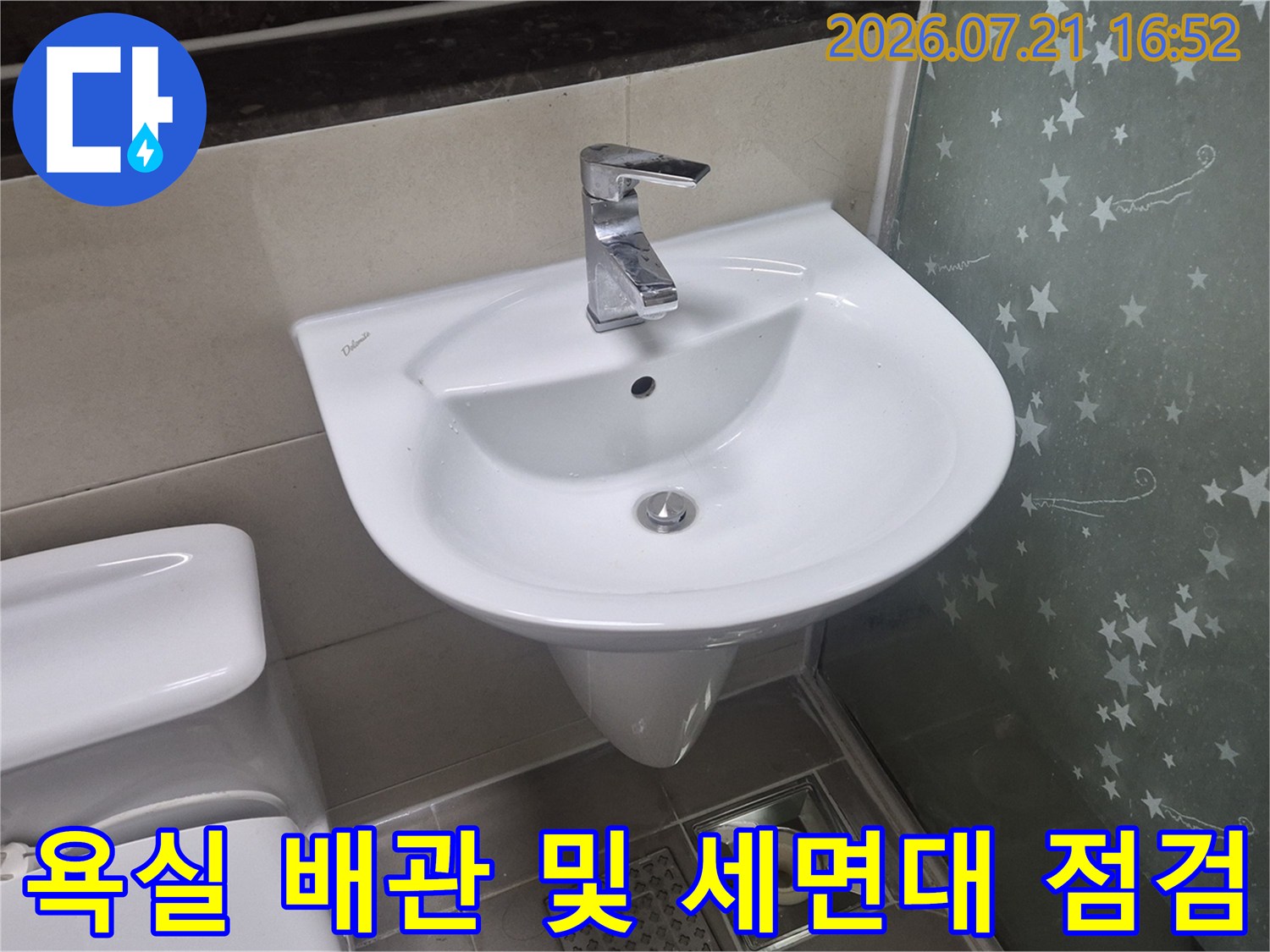 흰색 세면대 아래에 위치한 회색 배수구와 수직으로 연결된 배관의 사진