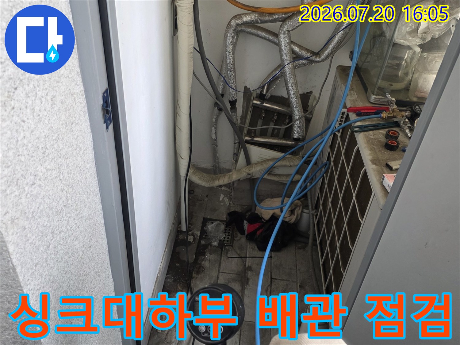 싱크대 하부 공간에서 복잡한 수도 및 가스 배관을 정밀하게 점검하는 모습