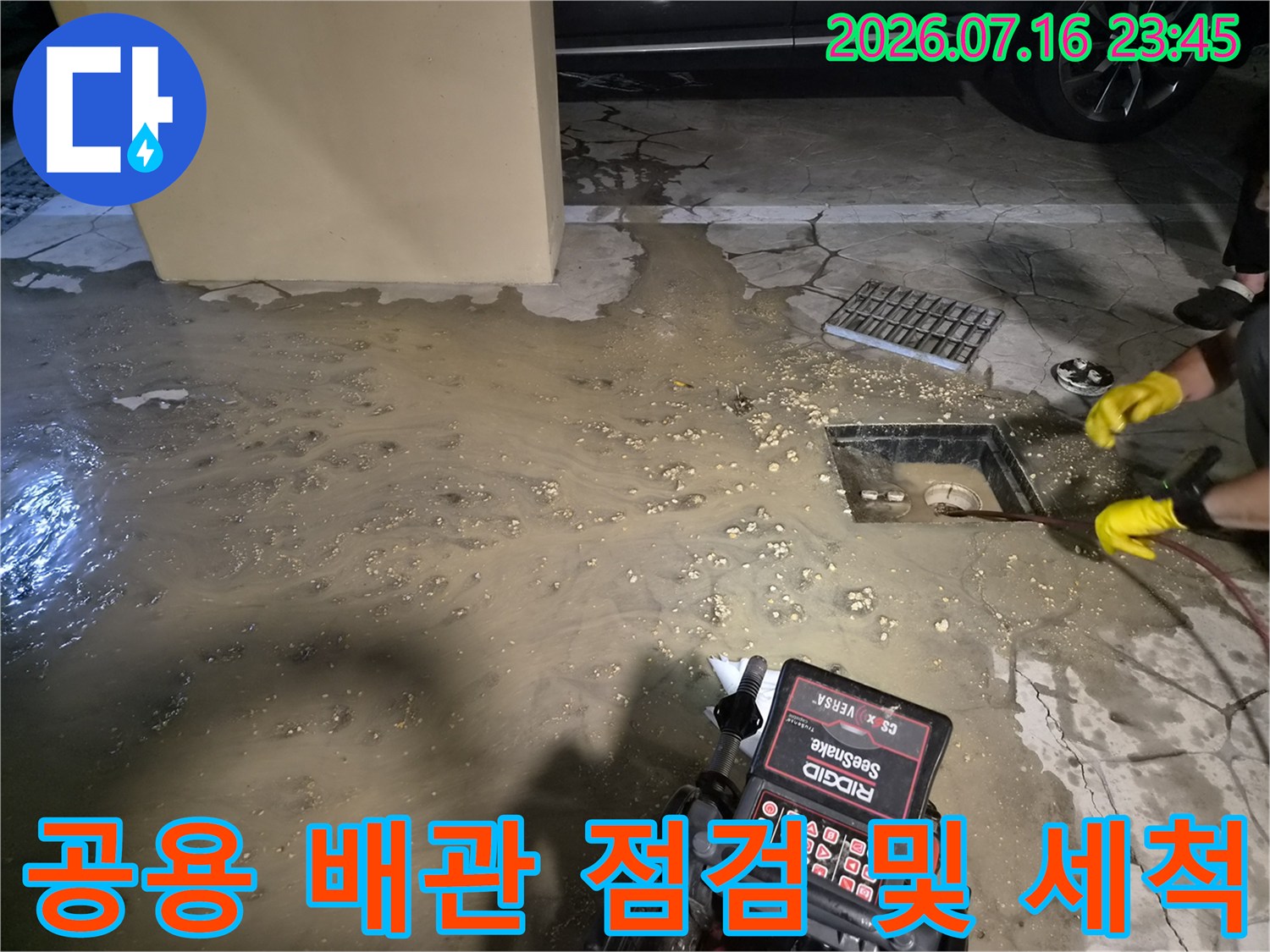 지하 공간에서 오수가 고인 상태의 배수구를 점검하고 막힌 부분을 제거하는 모습입니다.