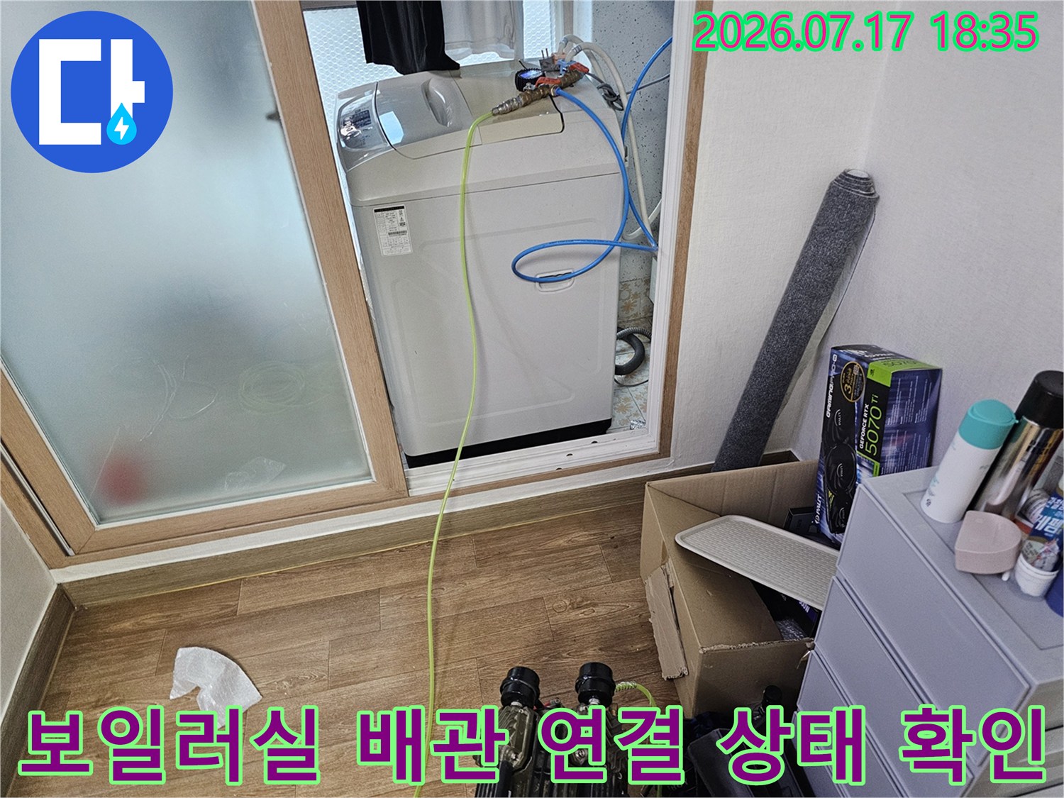 흰색 보일러 상단에 파란색과 노란색 호스가 복잡하게 연결된-배관 모습