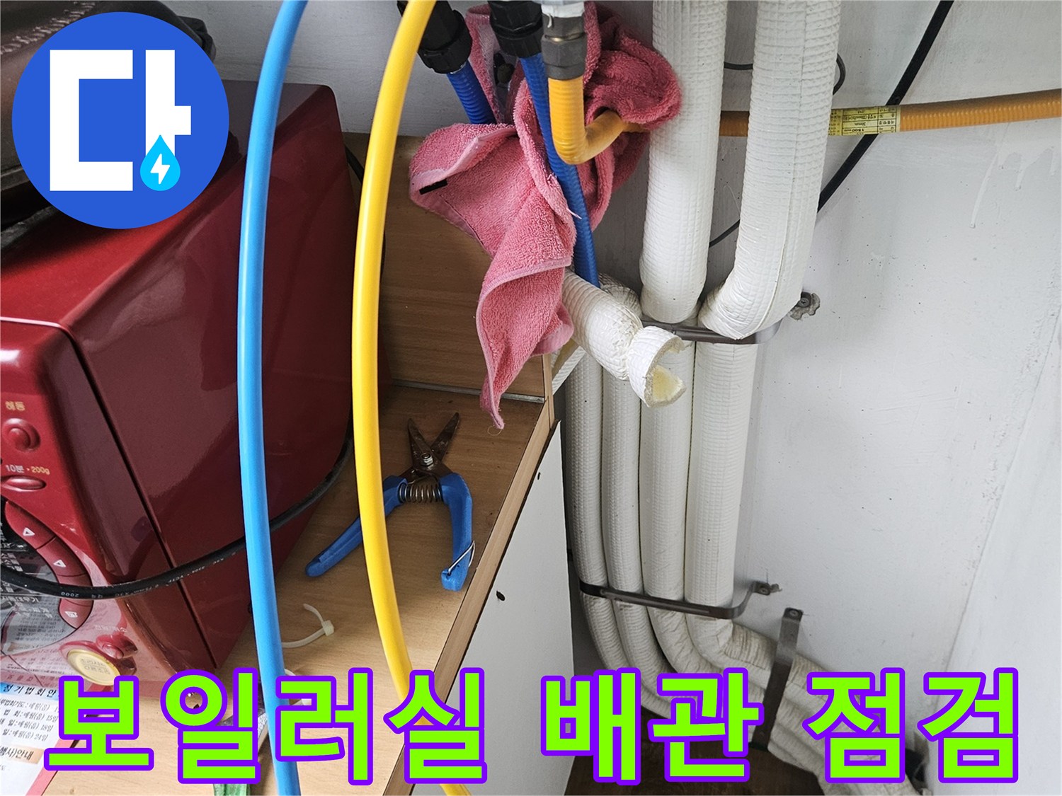 보일러실에 설치된 흰색 보일러와 연결된 노란색 및 파란색 배관의 모습입니다.