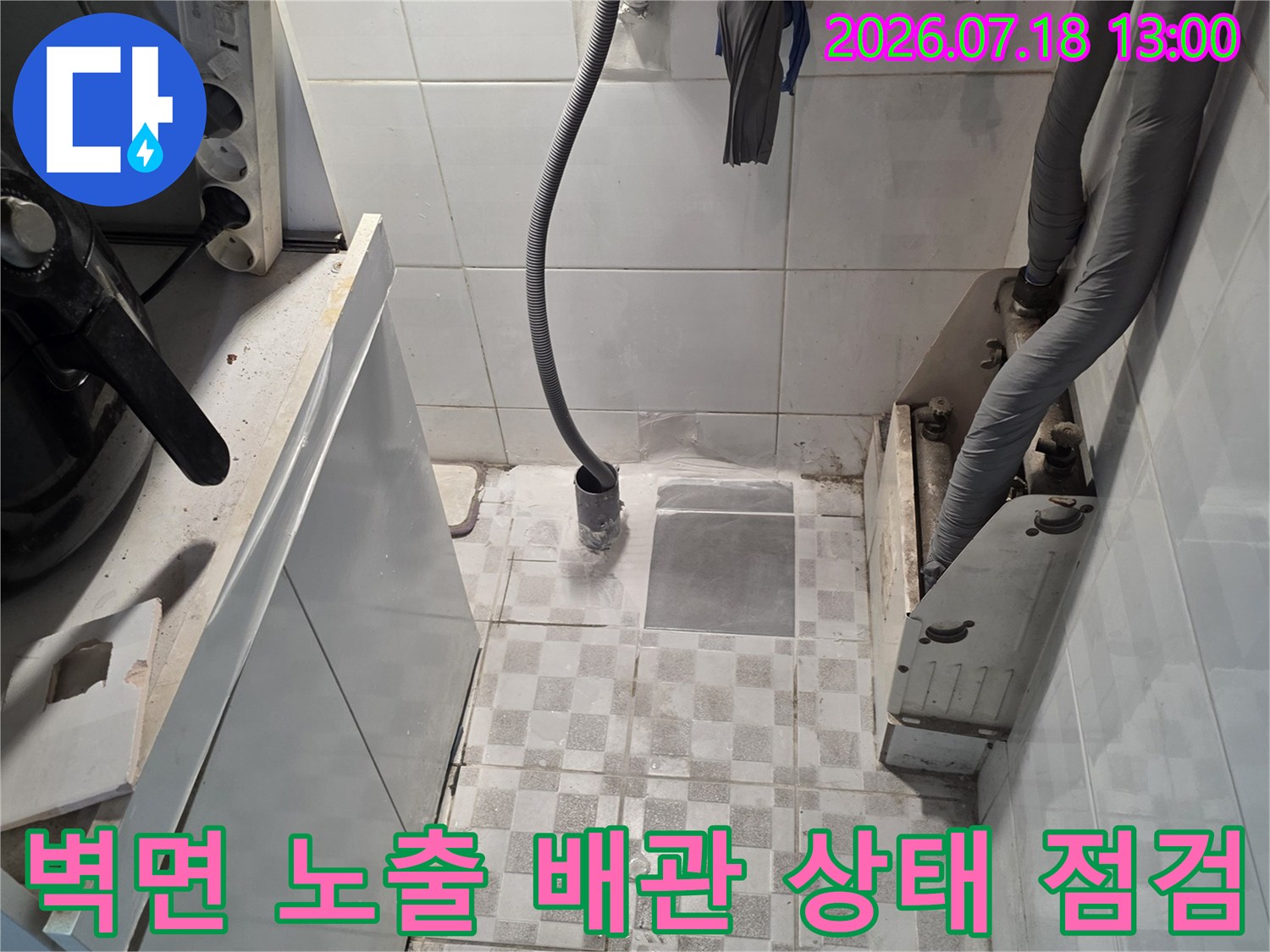회색 보온재 처리된 관과 노란색 호스가 타일 벽에 고정된 모습