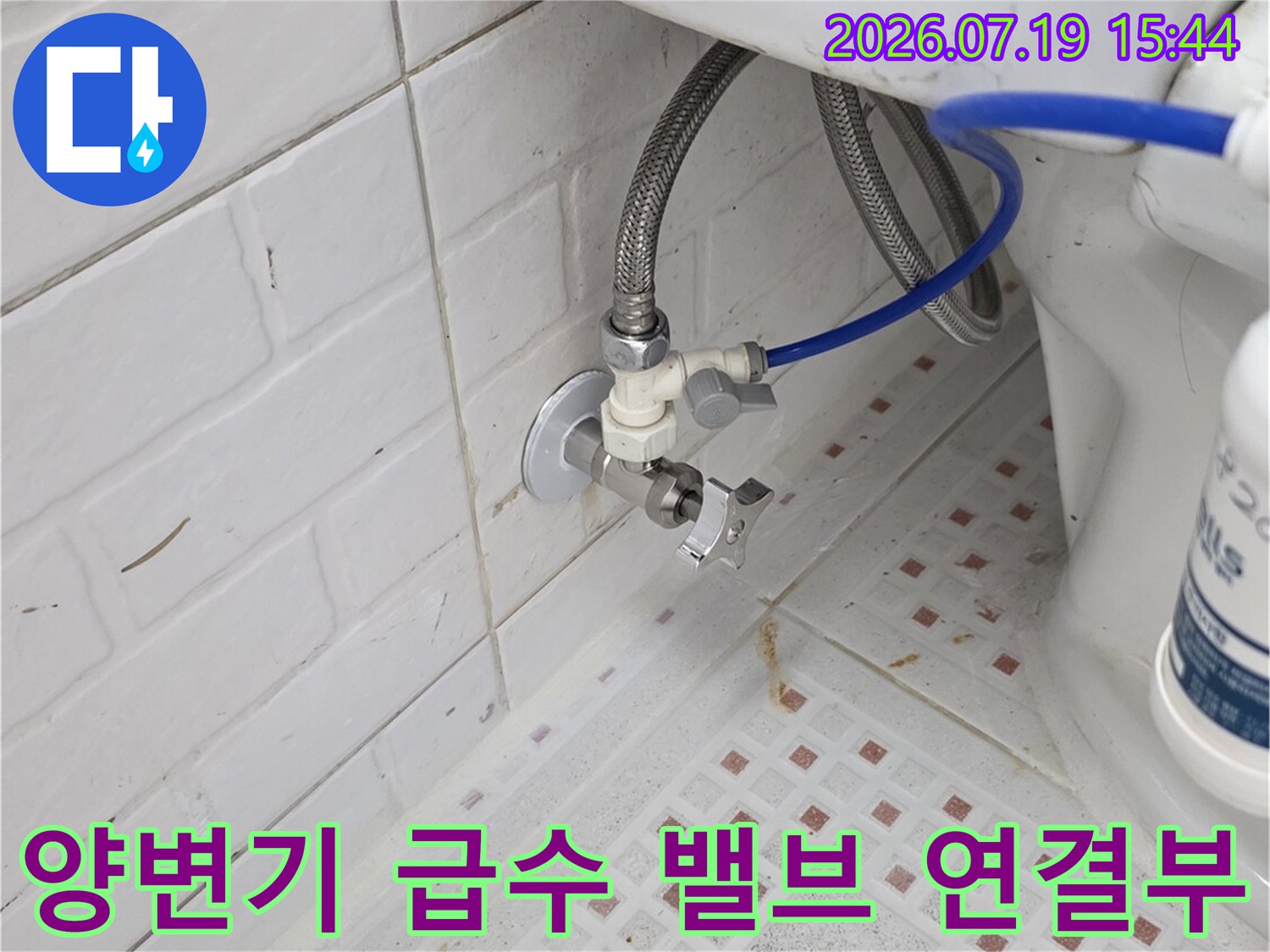 벽면 타일에 고정된 변기 급수 밸브와 아래로 이어지는 파란색 호스 사진