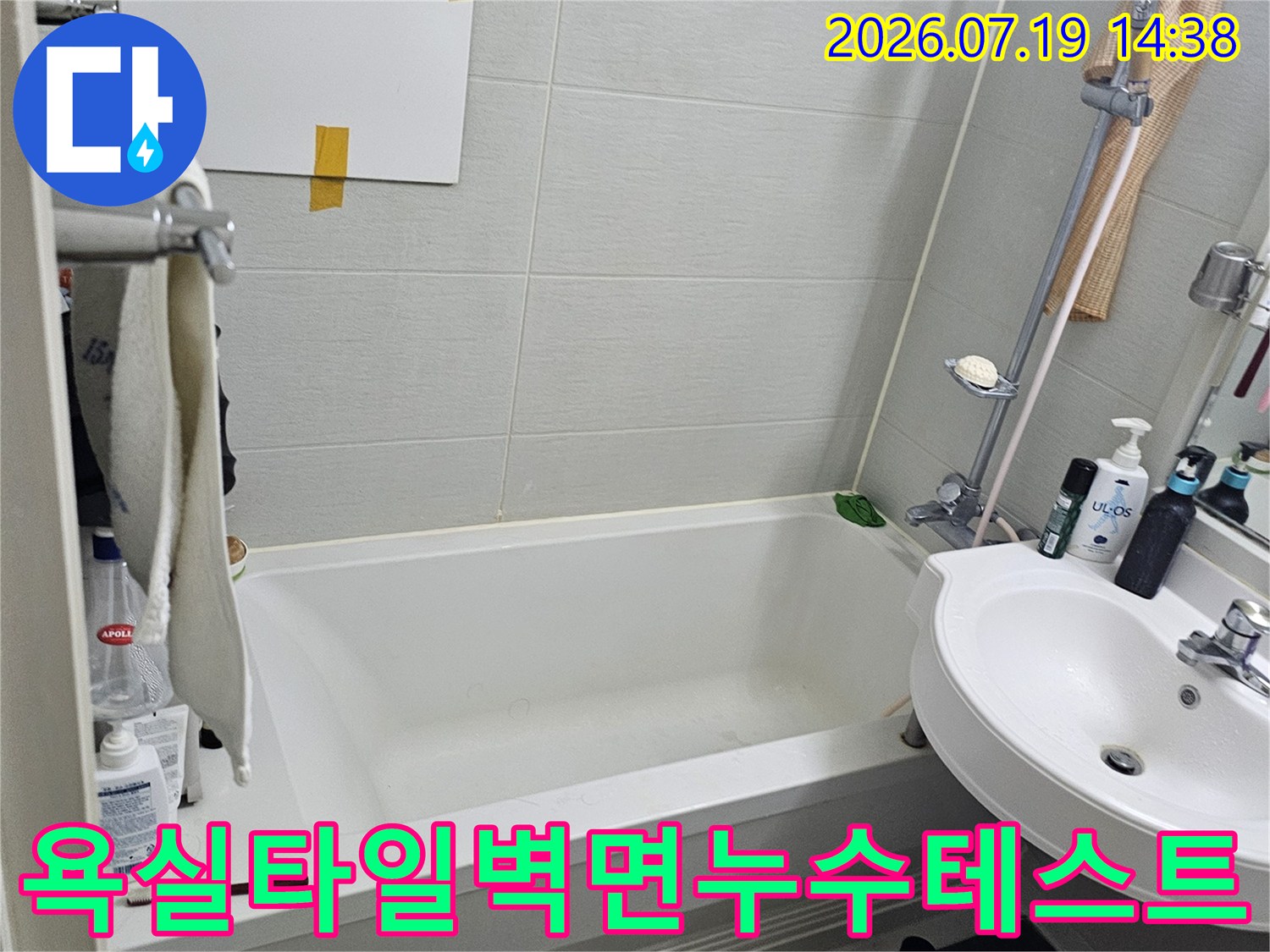 흰색 욕조와 세면대가 있는 욕실에서 벽면에 하얀 판을 붙여 누수를 테스트하는 모습