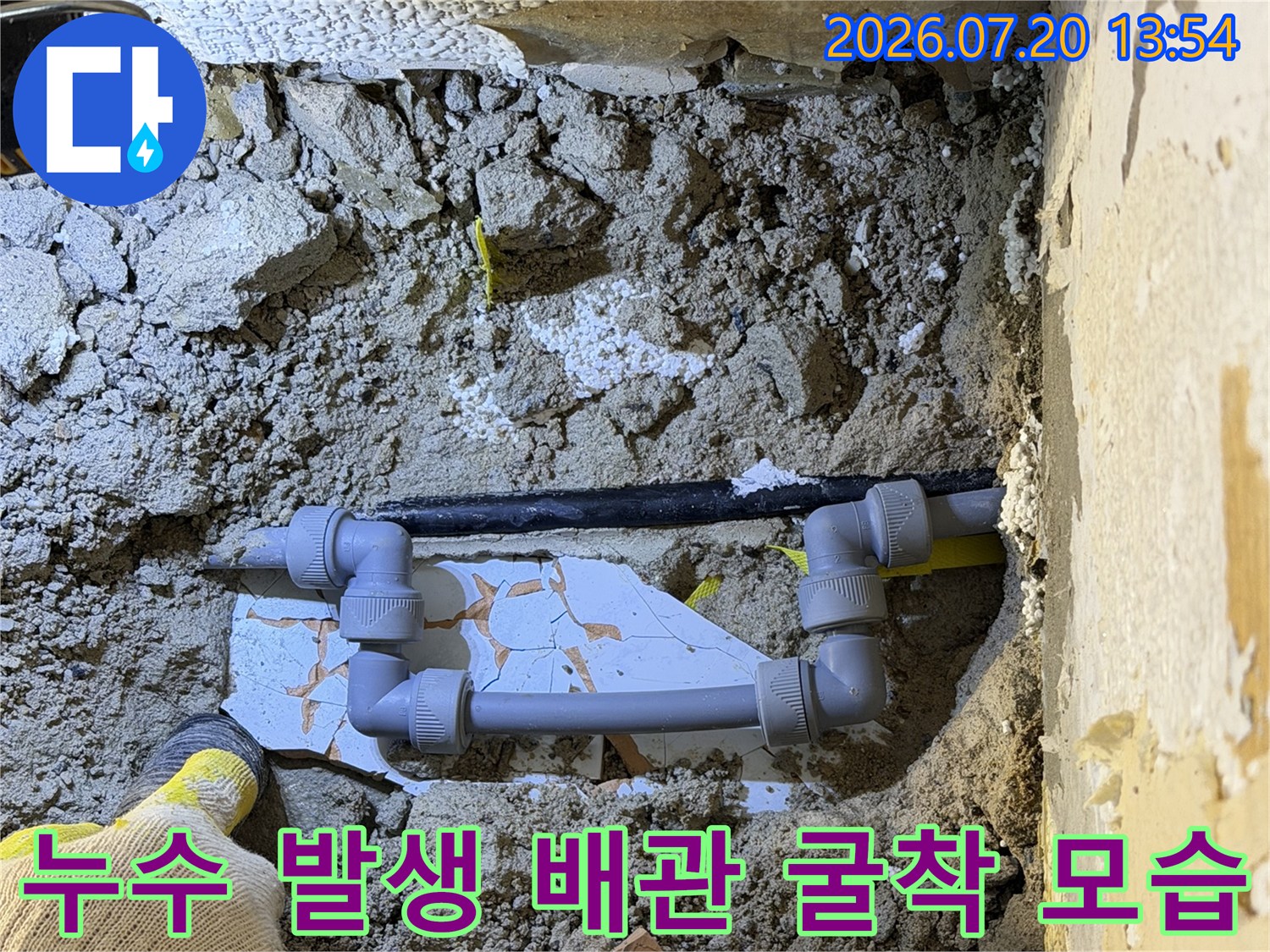 회색 플라스틱 파이프의 연결 부위-작업용 장갑을 낀 손과 주변 토사