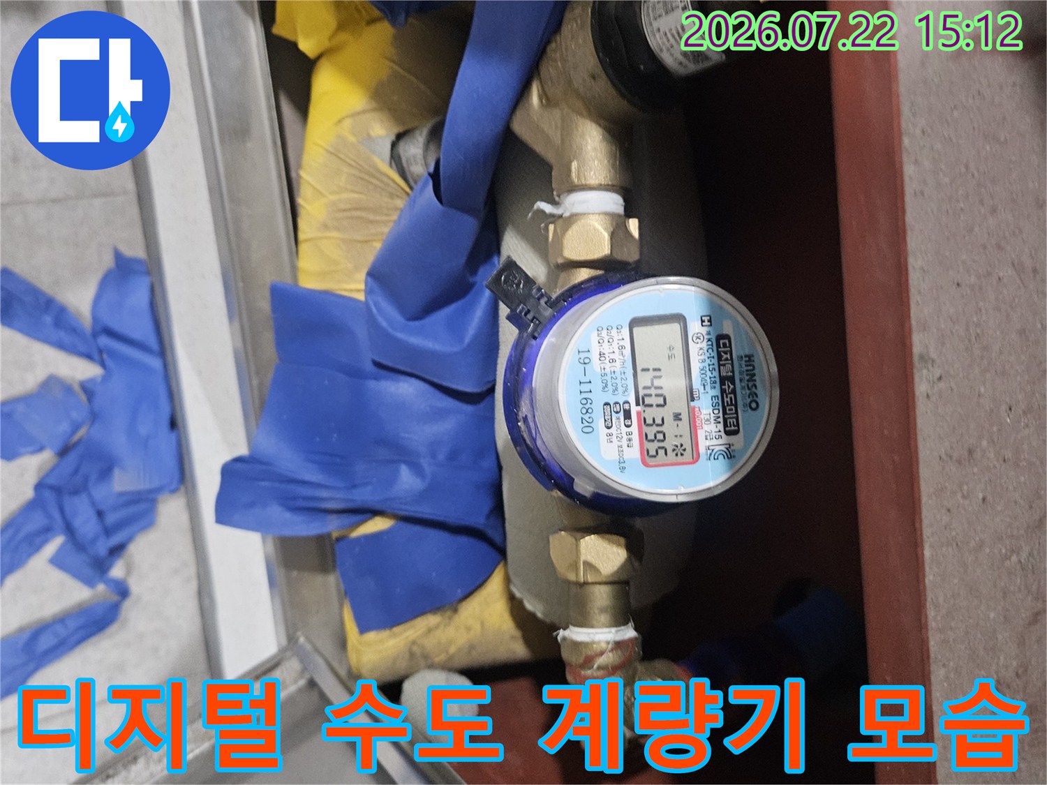 배관 연결 부위와 디지털 숫자가 표시된 수도 계량기가 설치된 모습-파란색 테이프 마감