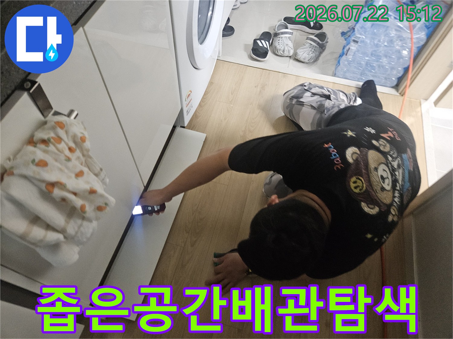 손전등을 사용하여 세탁실 하단부의 어두운 틈새를 세심하게 살피고 있는 작업자