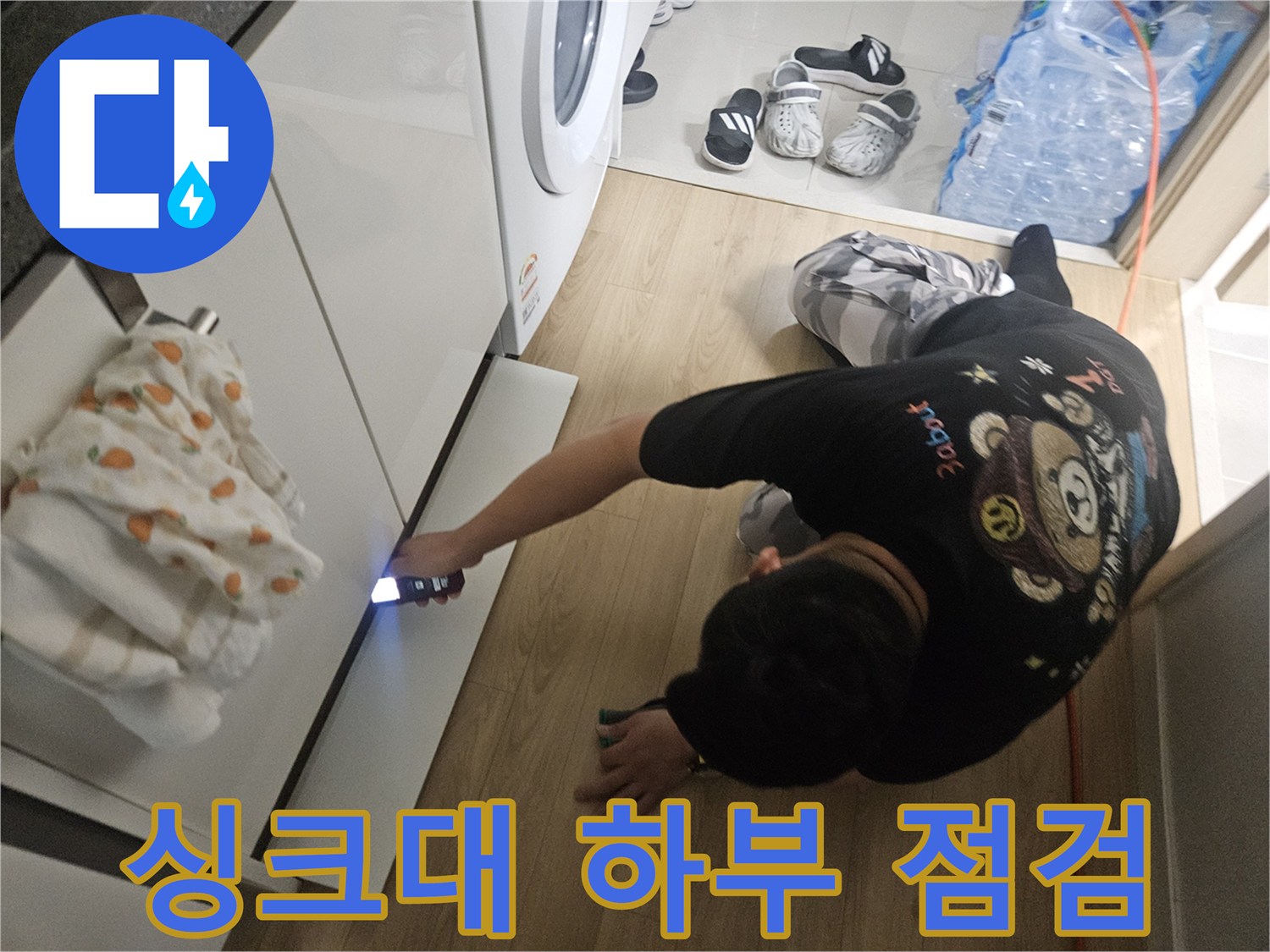 싱크대 아래쪽 좁은 공간을 손전등으로 비추며 배관 상태를 확인하는 모습