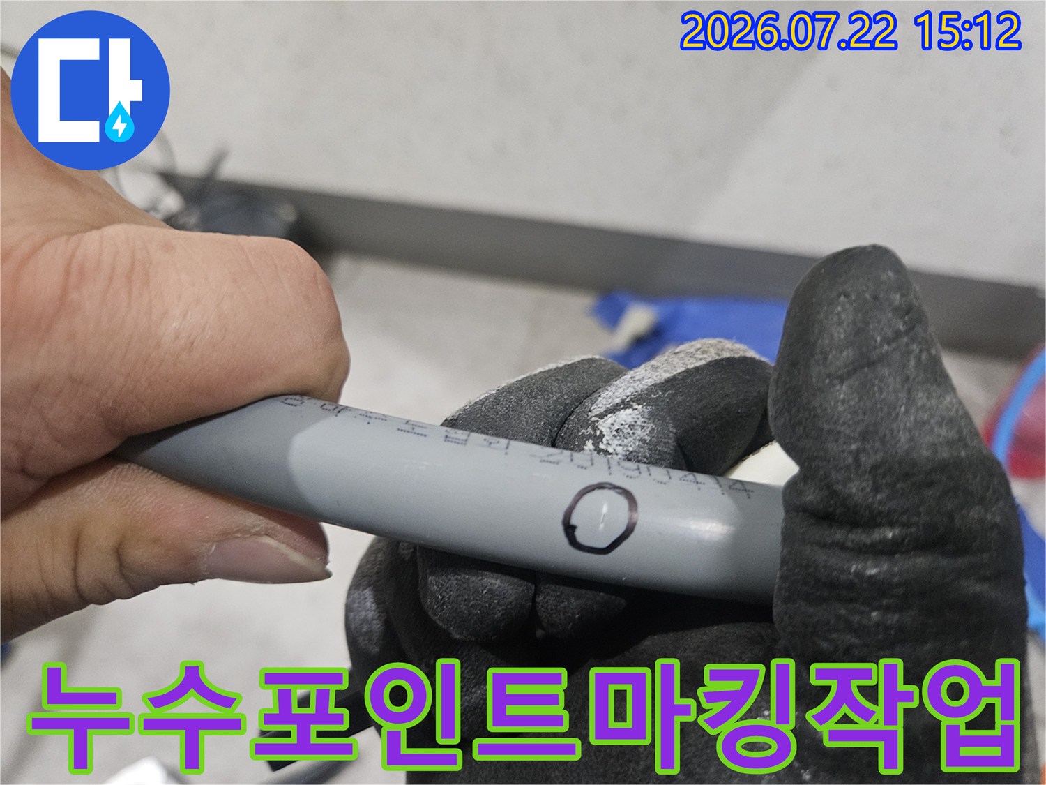 작업용 장갑을 낀 손이 회색 배관 위에 검은 원으로 표시된 누수 지점을 가리키는 사진