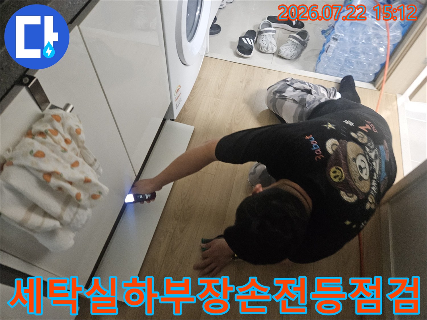 작업자가-세탁실-싱크대-하단-좁은-공간에-손전등을-비추어-배관-상태를-확인하는-모습