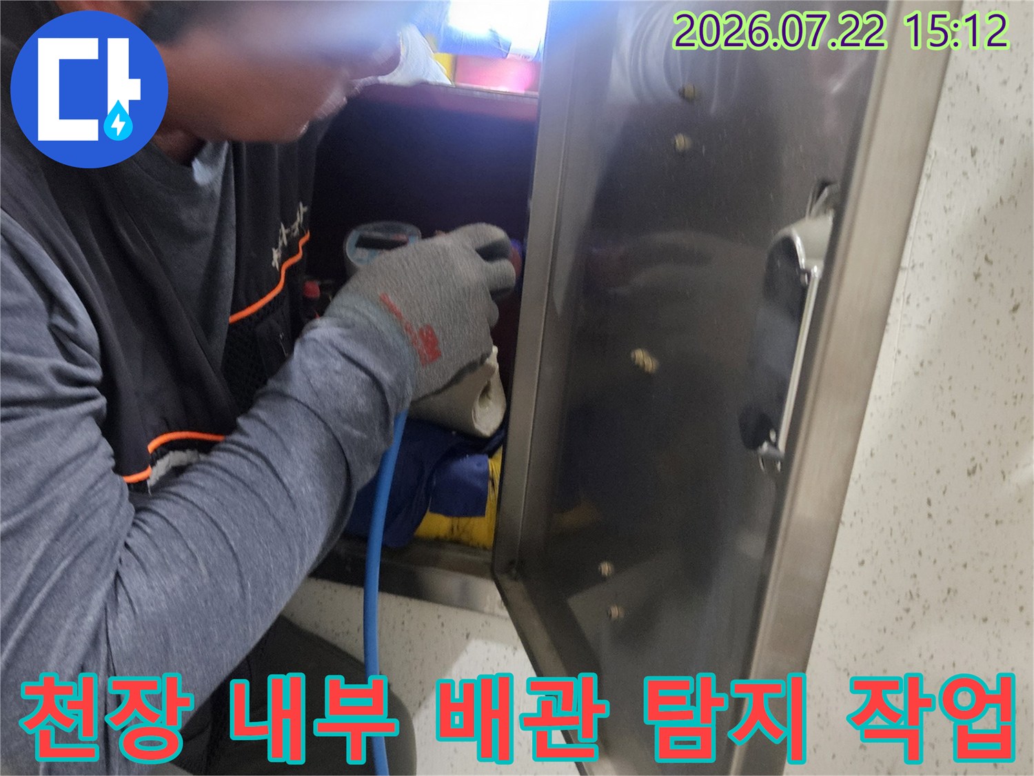 작업자가 좁은 천장 공간에서 파란색 호스가 연결된 장비를 이용해 누수를 점검하는 모습
