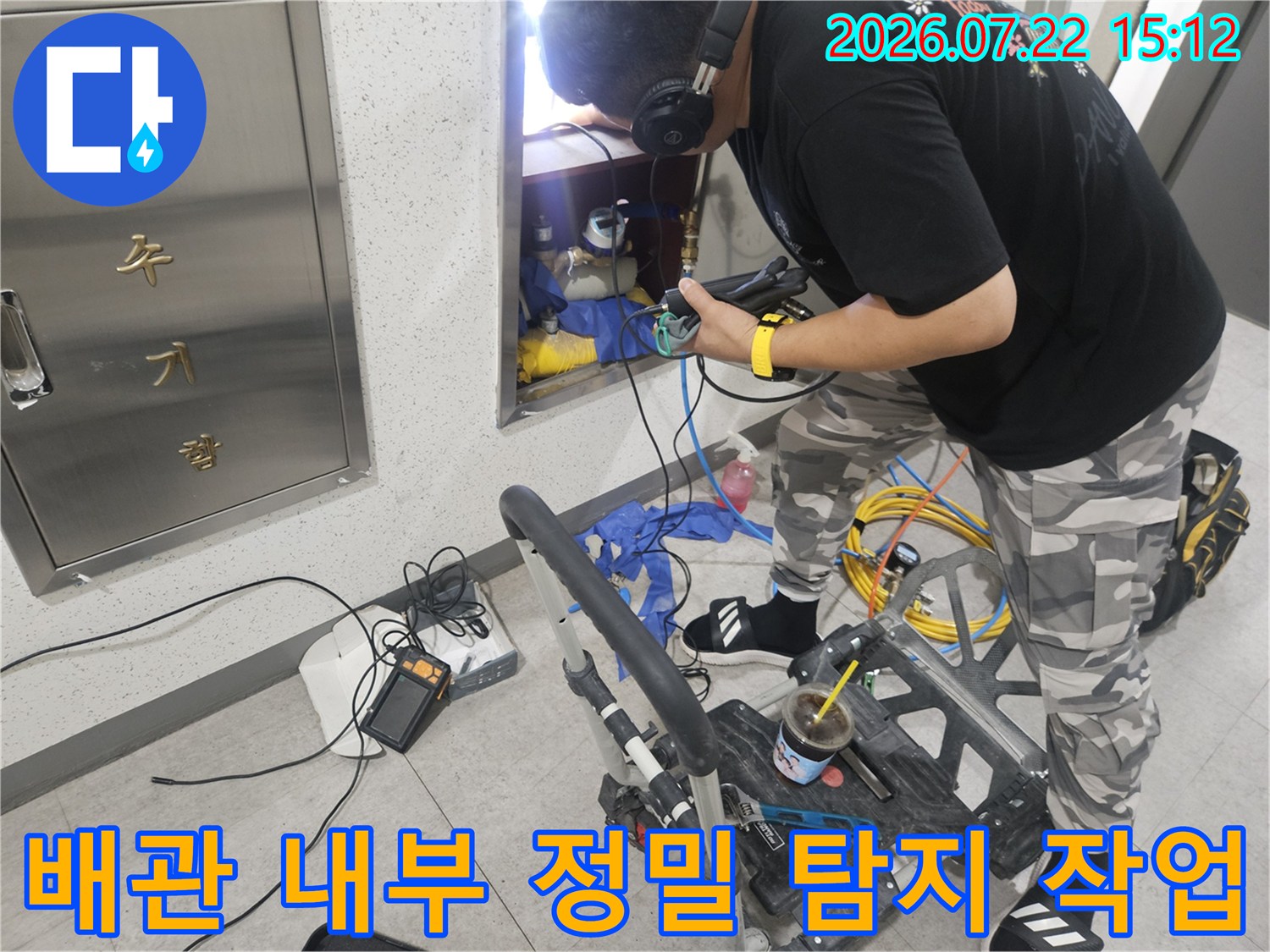 작업자가 헤드셋을 착용하고 배관 함 내부에 전용 탐지 장비를 넣어 누수 지점을 찾는 모습