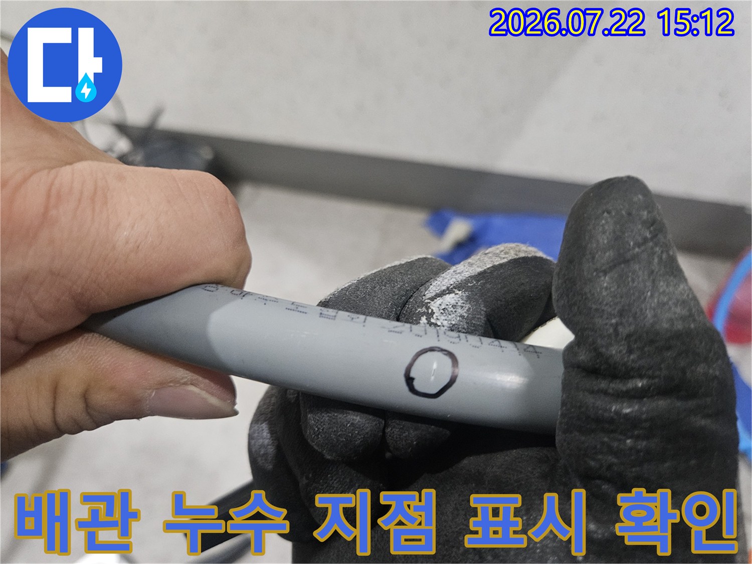 작업자가 회색 배관의 특정 부위에 검정색 펜으로 동그라미를 그려 누수 지점을 표시하고 있는 모습