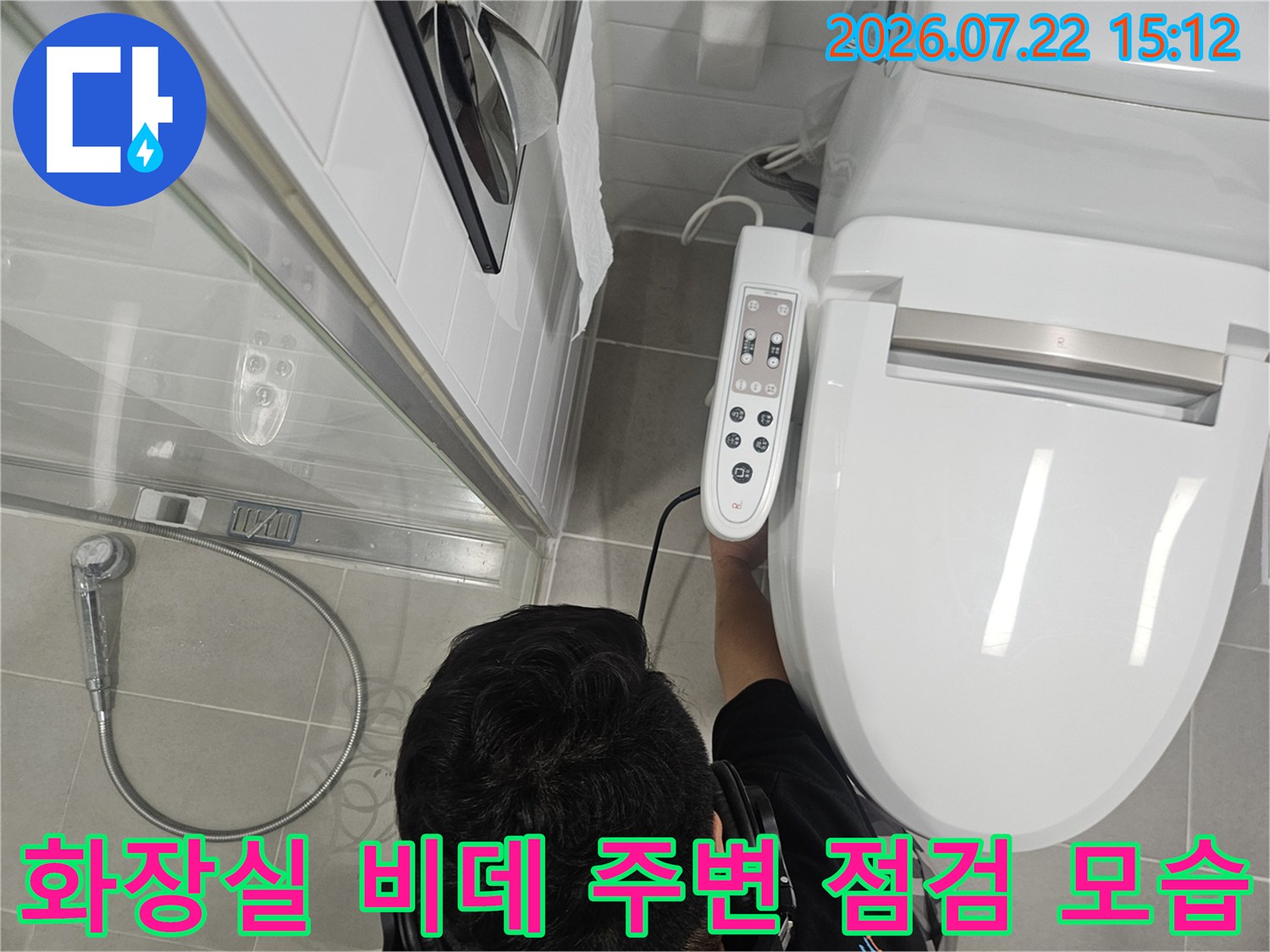 화장실 내 설치된 전자 비데의 조작 패널과 배관 연결 부위를 살피고 있는 엔지니어의 모습